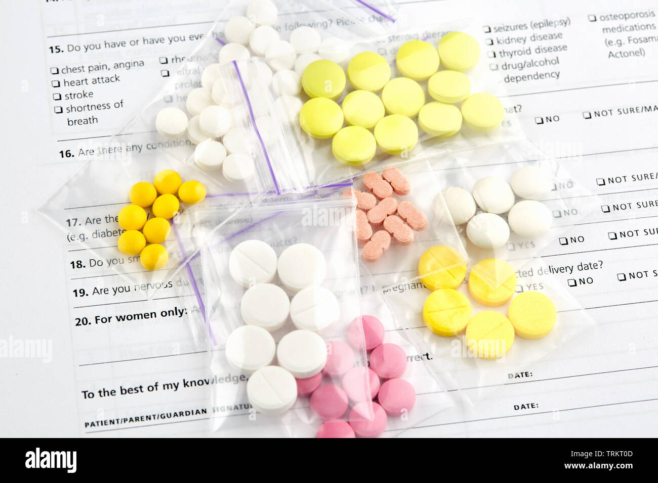 Rose, blanc et jaune comprimés dans des sacs en plastique sur le questionnaire médical formulaire. Banque D'Images