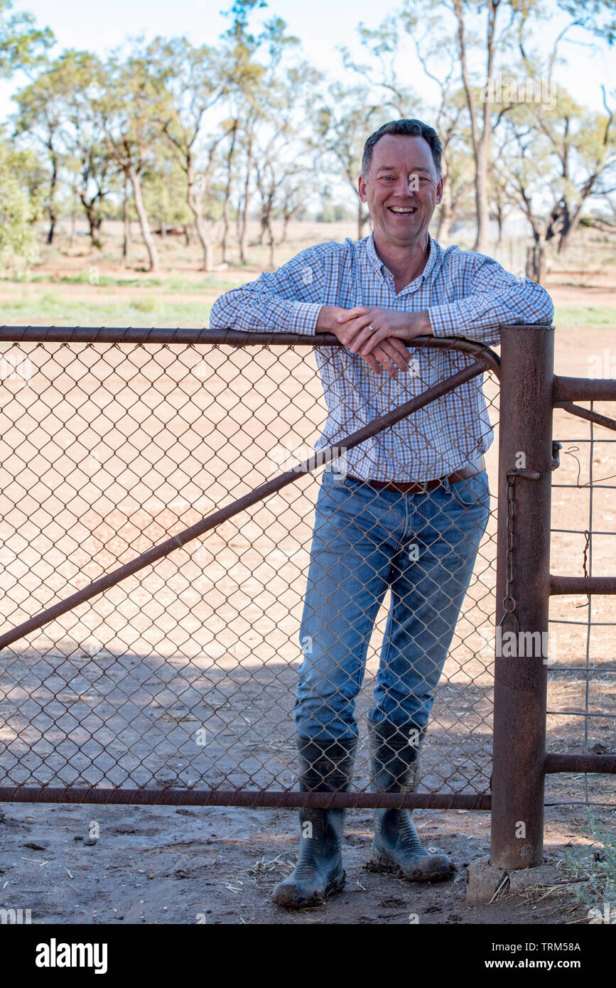 Un homme de l'Australie blanche personne souriante (fin des années 50) debout face à un pays, s'appuyant sur la porte en jeans, un polo shirt et gomme (caoutchouc) boots Banque D'Images