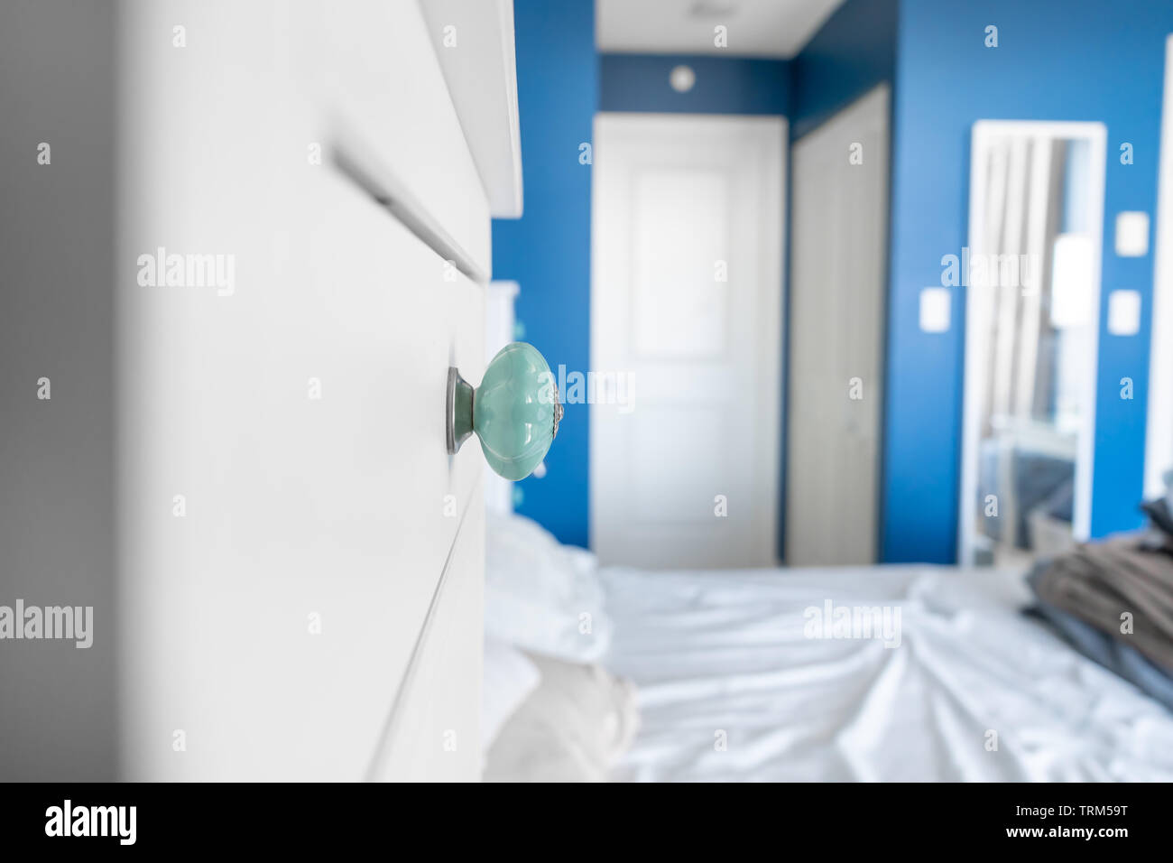 Vue en perspective d'une chambre montrant un bouton de dresser des murs peints en bleu, blanc, accents et un lit sans couvertures, avec des draps froissés, malpropre. Banque D'Images