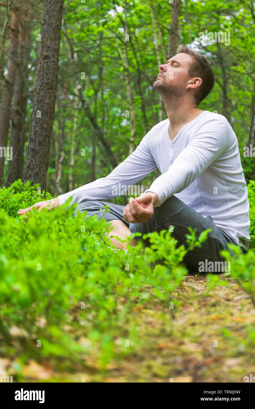 Mid adult man s'asseoir à l'extérieur seul avec yeux fermés méditant dans une luxuriante forêt verte fraîche typique en pose détente Banque D'Images