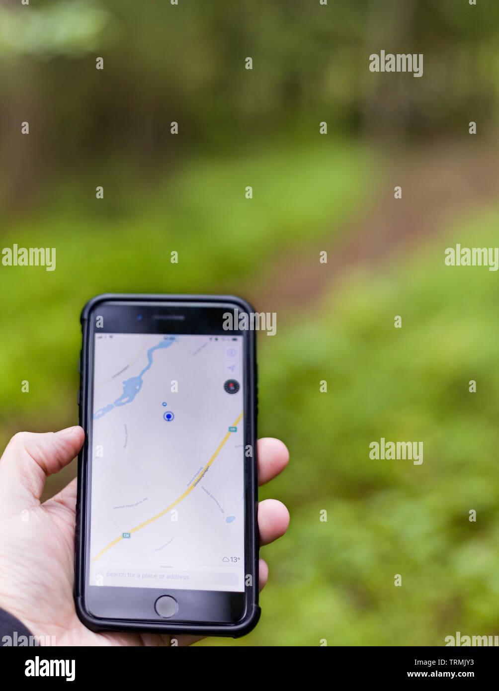 Personne holding smartphone avec une main avec la carte open app d'essayer de trouver le moyen d'un chemin ou sentier de randonnée en forêt à l'extérieur Banque D'Images