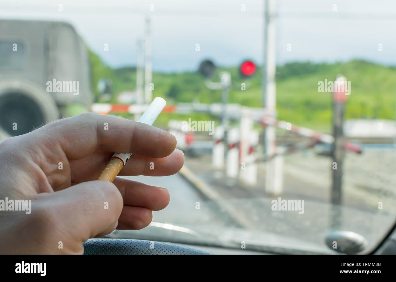 Vue de la part du pilote avec une cigarette sur le volant de la voiture,  qui s'est arrêté devant un passage à niveau fermé à un feu rouge Photo  Stock