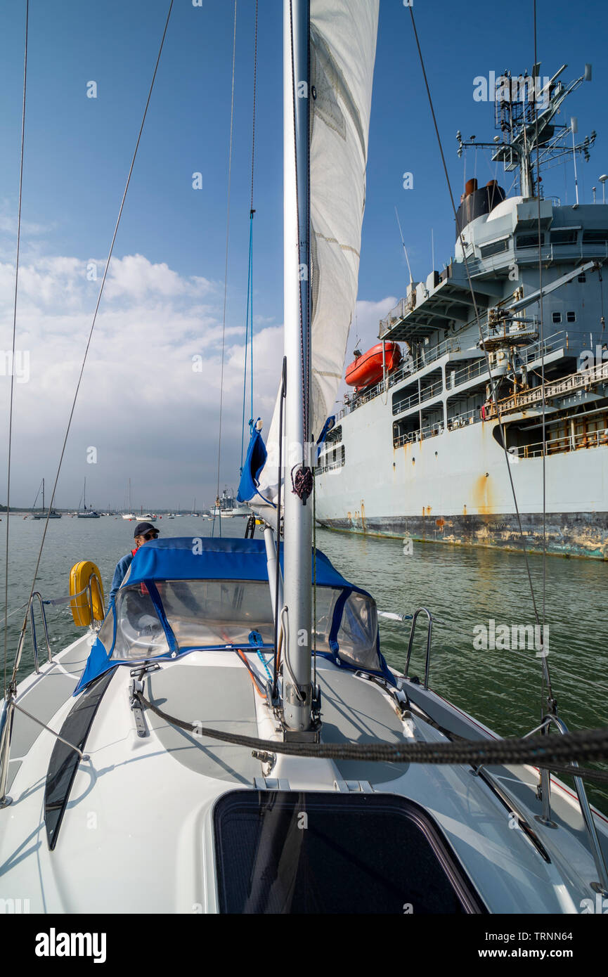 Yacht à voile en passant par la Marine royale, un navire amarré dans le port de Portsmouth Banque D'Images