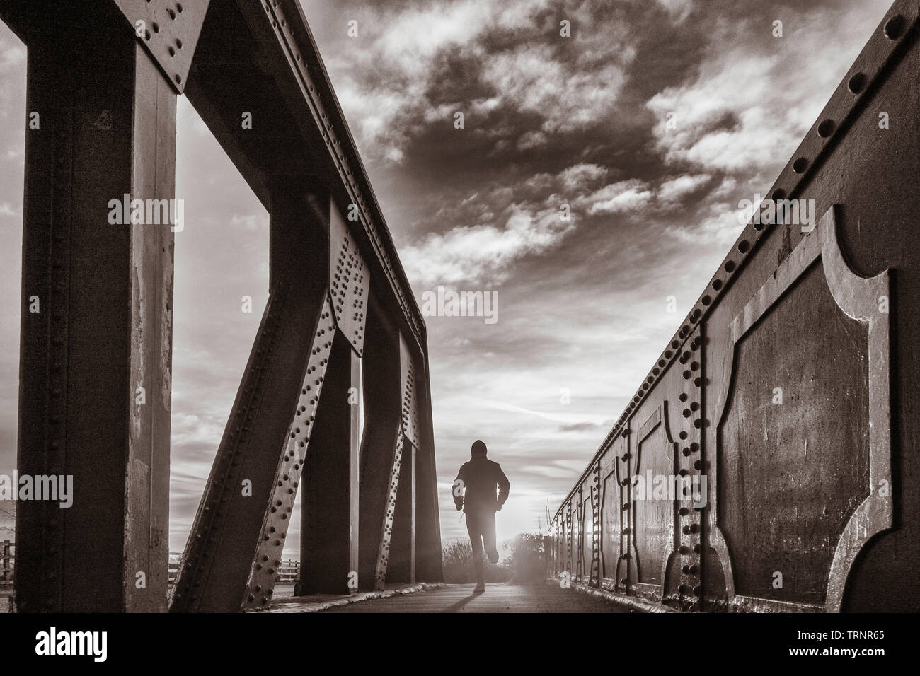 Vue arrière de l'homme fonctionnant sur Bridge au lever du soleil. UK Banque D'Images