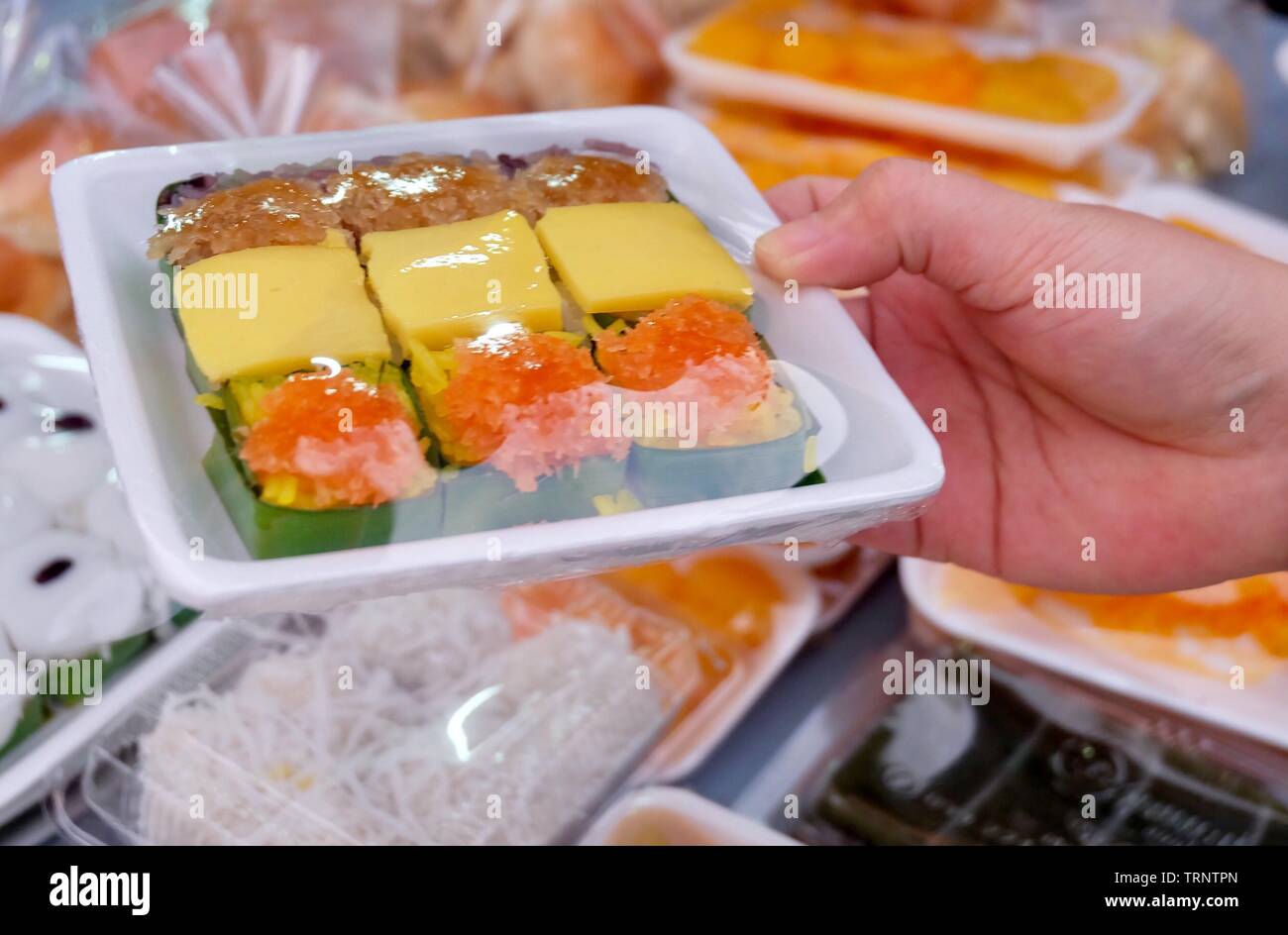 Dessert traditionnel thaï, main tenant le riz gluant sucré garni d'oeufs cuits à la crème anglaise, du poisson séché et des crevettes frites dans un coffret plastique. Banque D'Images