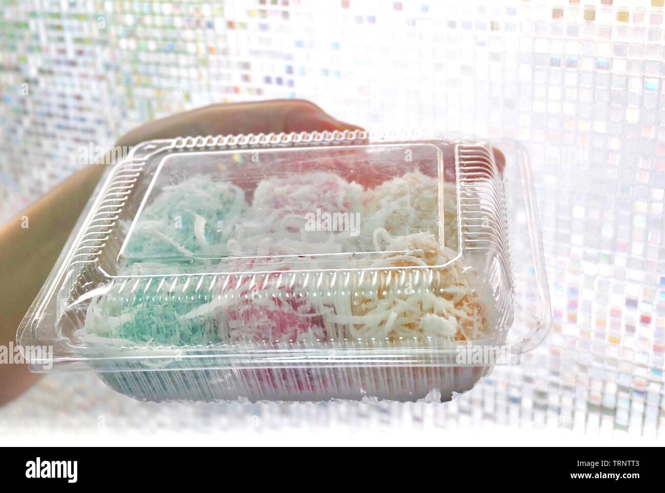 Dessert traditionnel thaï, main tenant Thai Coconut Muchkins colorés ou Boules de riz gluant farci de noix de coco sucrée dans un coffret plastique. Banque D'Images