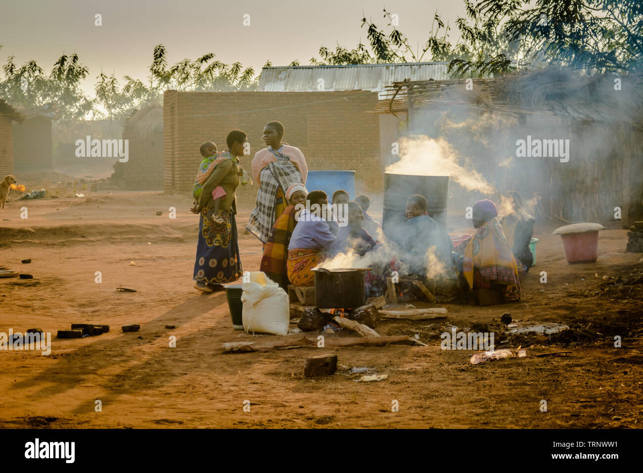 Les femmes se rassemblent autour d'énormes pots d'eau bouillante dans un village du Malawi au coucher du soleil Banque D'Images