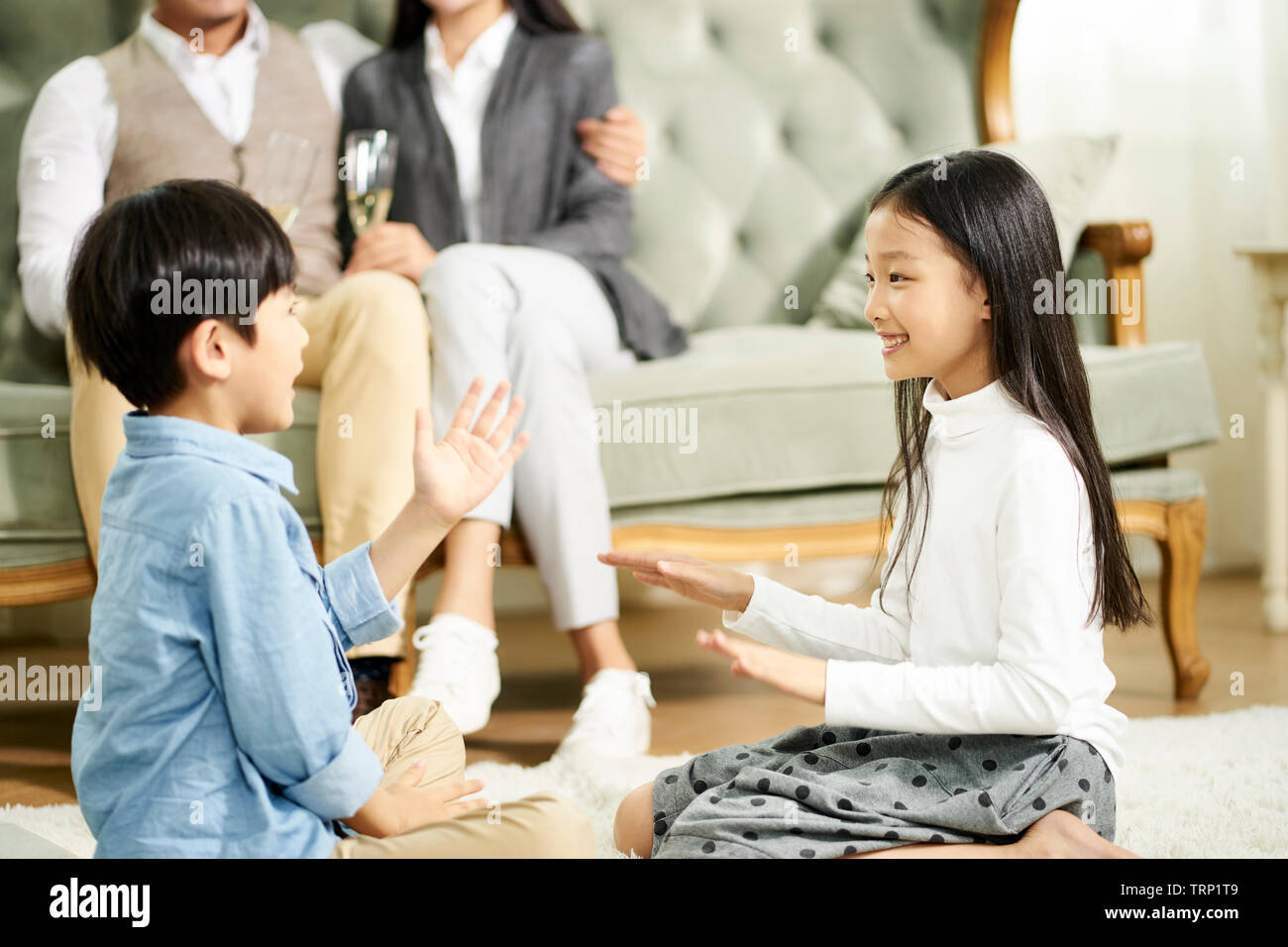 Frère et soeur asiatique assis sur un tapis de jouer pendant que les parents regardent en arrière-plan Banque D'Images