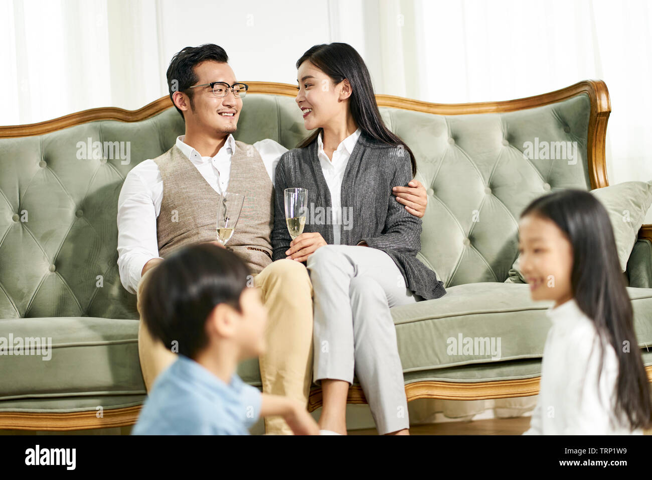 Frère et soeur asiatique assis sur un tapis à jouer tandis que les parents de discuter en arrière-plan, l'accent sur les parents. Banque D'Images