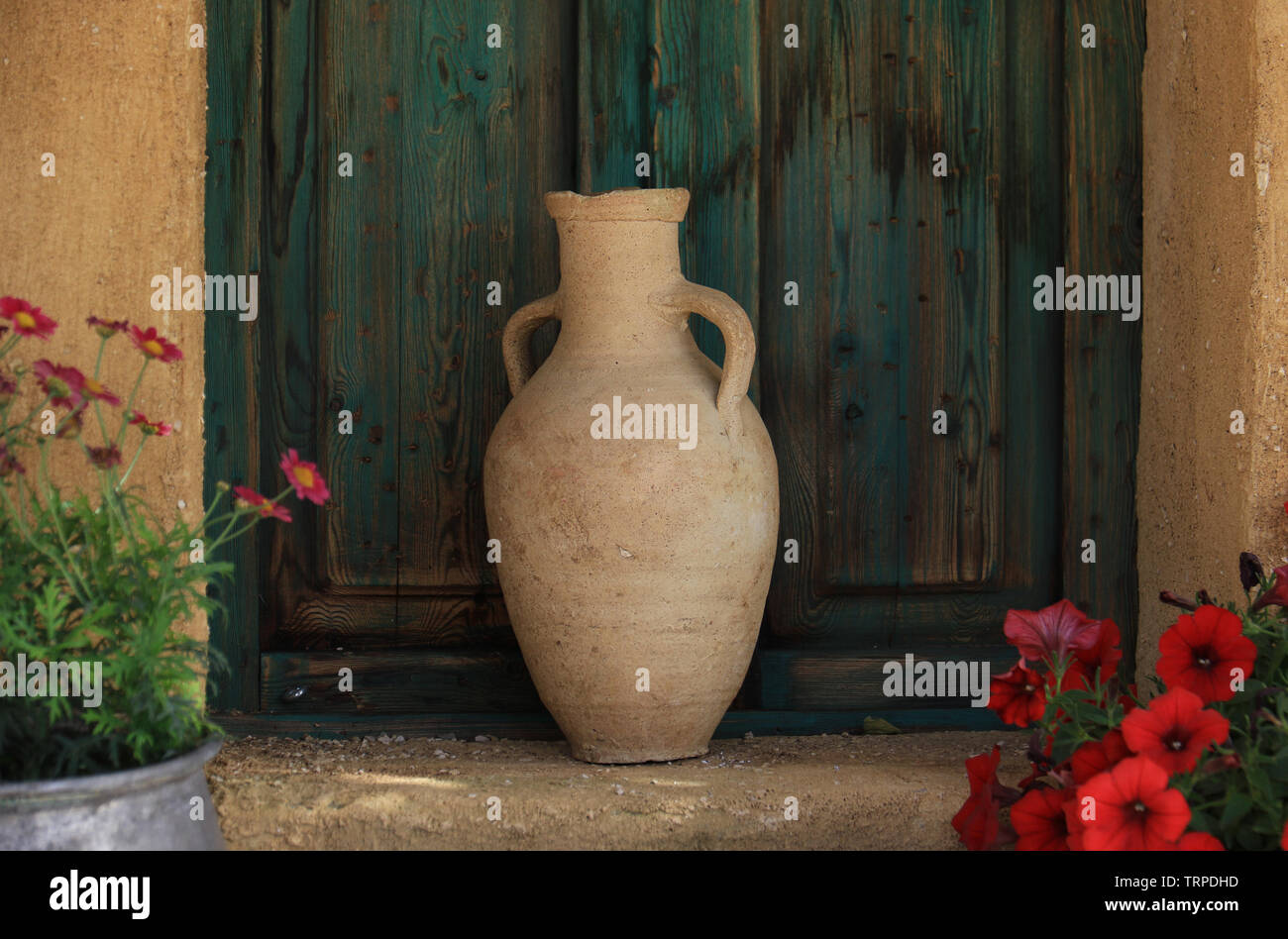 Un pot en terre cuite traditionnelle libanaise dans un jardin en face d'une ancienne fenêtre verte. Banque D'Images