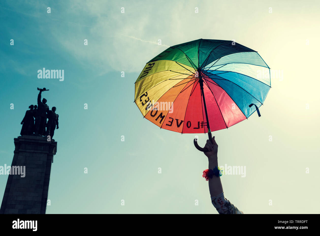 Human hand holding parapluie arc-en-ciel de la fierté dans le ciel à côté du monument de l'armée soviétique à Sofia Selective focus Banque D'Images