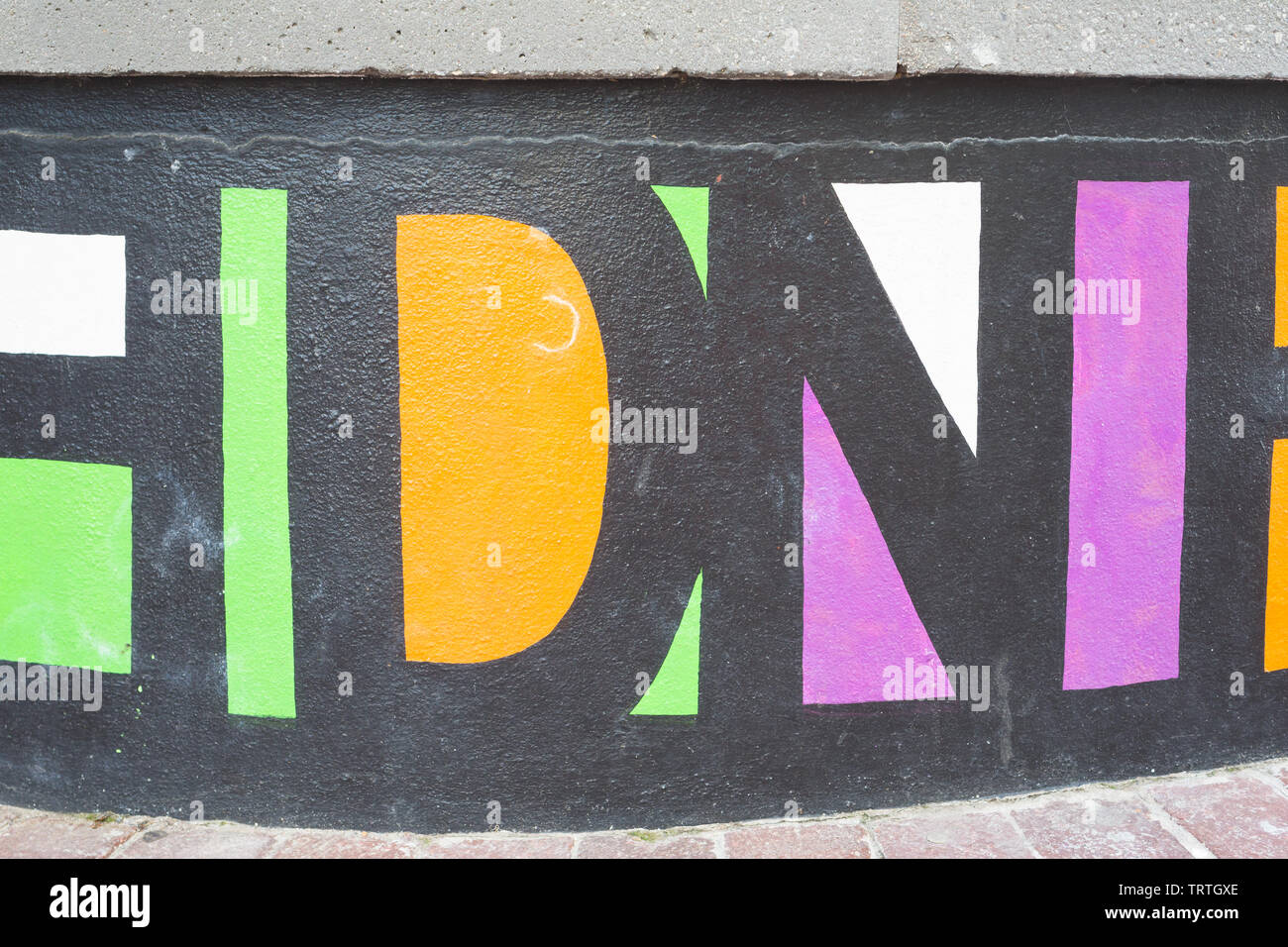 Les lettres majuscules ou texte peint en peinture noire avec des couleurs éclatantes des espaces de remplissage sur le béton mur incurvé dans un environnement urbain en Afrique Banque D'Images