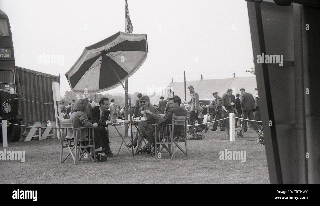 Années 1950, tableau historique de deux couples assis dehors à une table de jardin avec plateau et socialiser ensemble au comté de Bucks show, Hartwell Park, Aylesbury, Angleterre, Royaume-Uni. Banque D'Images