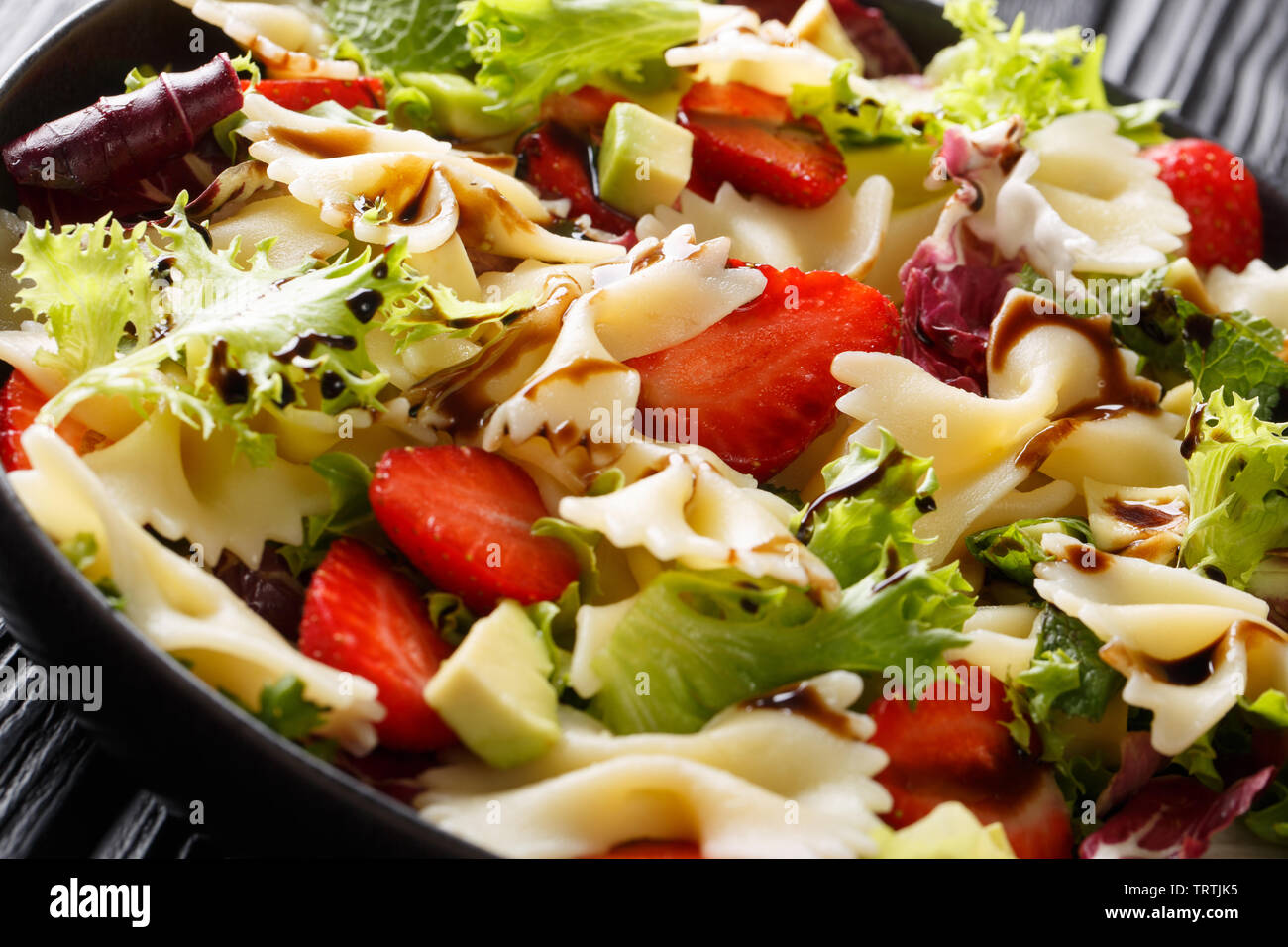 Pâtes Farfalle avec de l'avocat, de fraises, mélanger la laitue et vinaigrette balsamique close-up sur une plaque sur la table horizontale. Banque D'Images