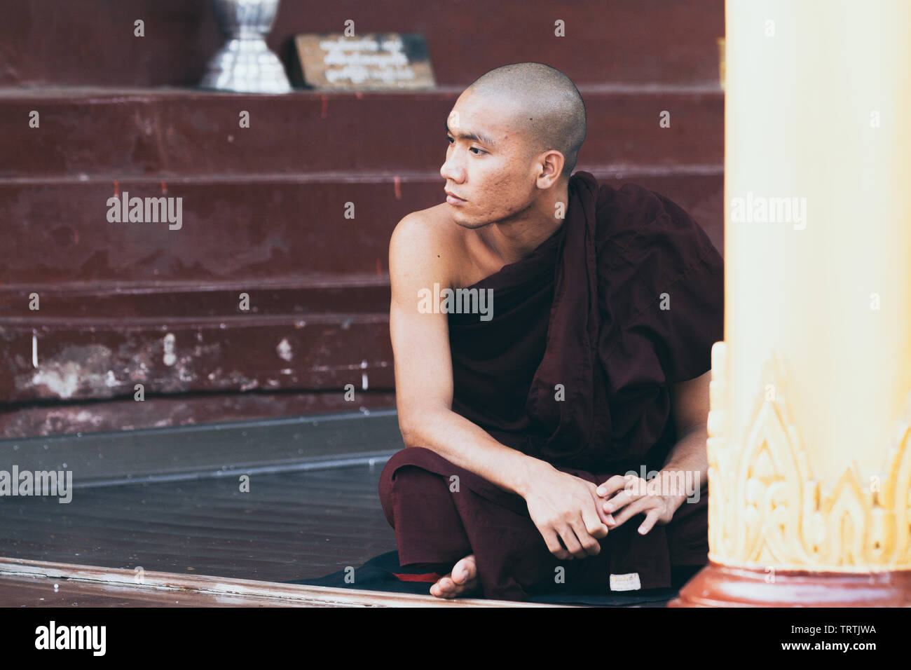 Yangon, Myanmar - Mars 2019 : portrait d'un jeune moine bouddhiste novice masculin assis dans le portique du temple de la pagode Shwedagon Banque D'Images