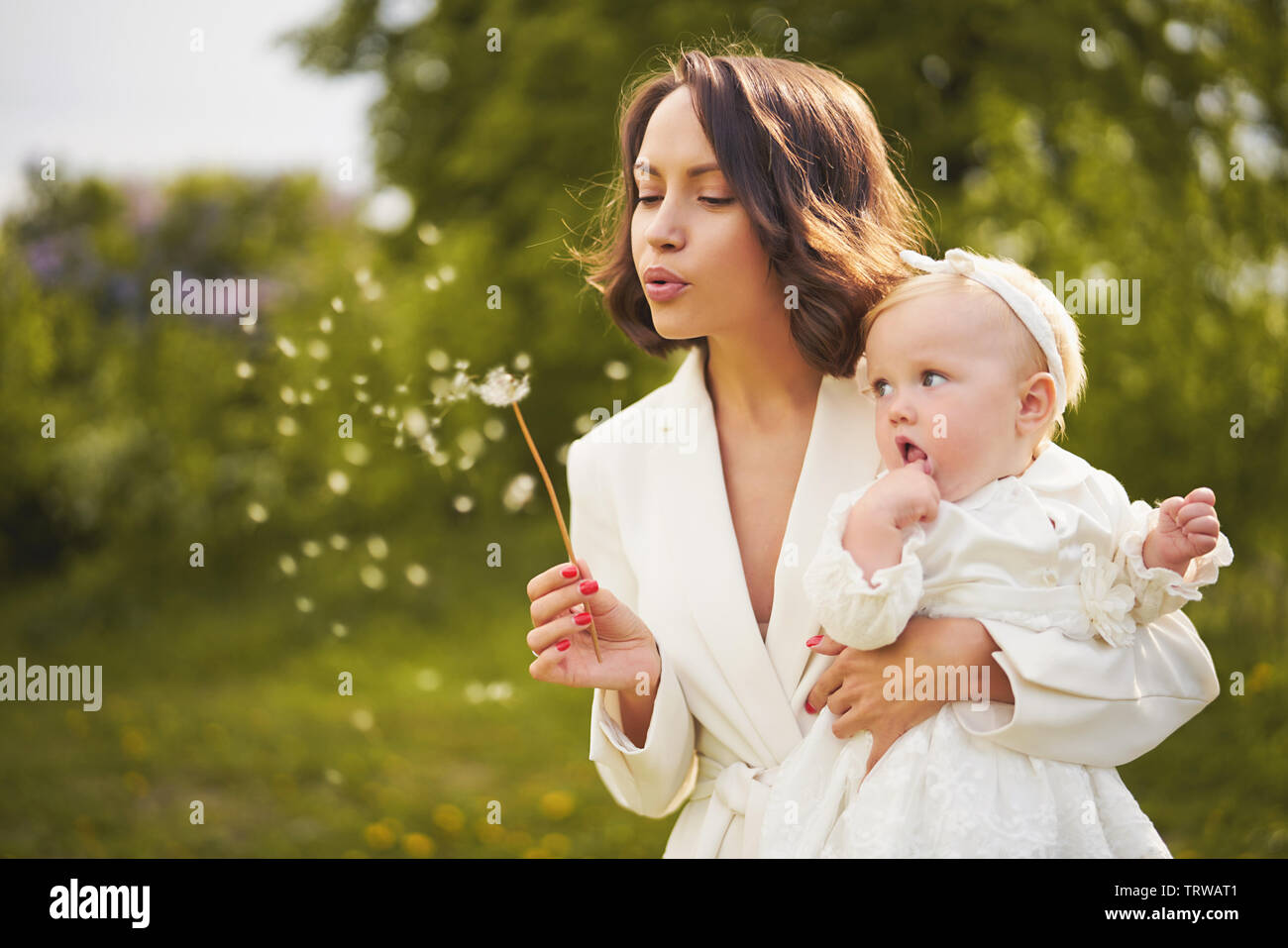 Piscine fashion portrait de jeune belle mère et fille mignon petit souffle de pissenlit sur le pré vert. Image d'été Banque D'Images