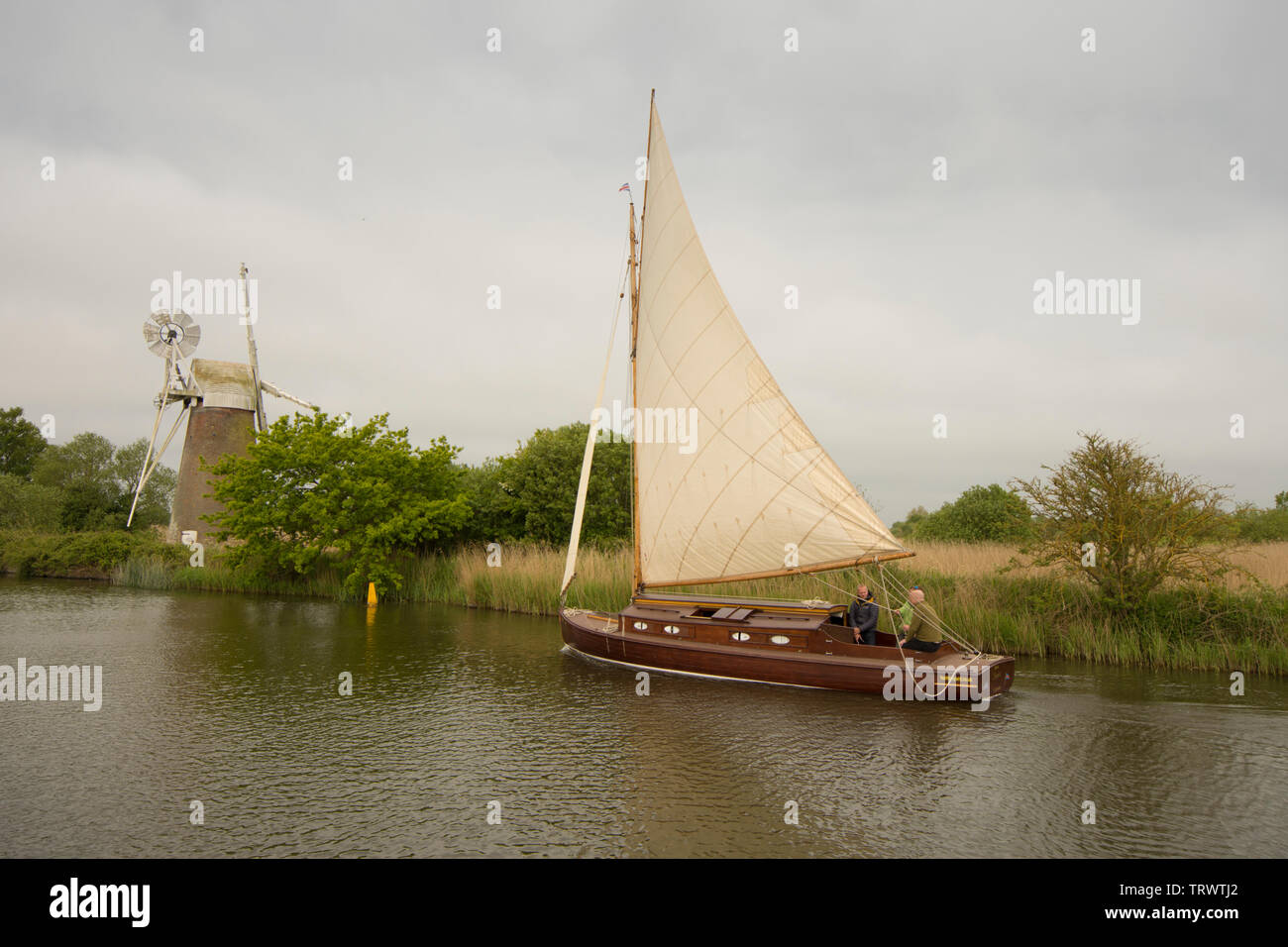 Trois hommes dans un bateau à voile sur la rivière à Ant en face de Turf Drainage Fen Moulin, comment Hill, Norfolk Broads, UK, Mai Banque D'Images