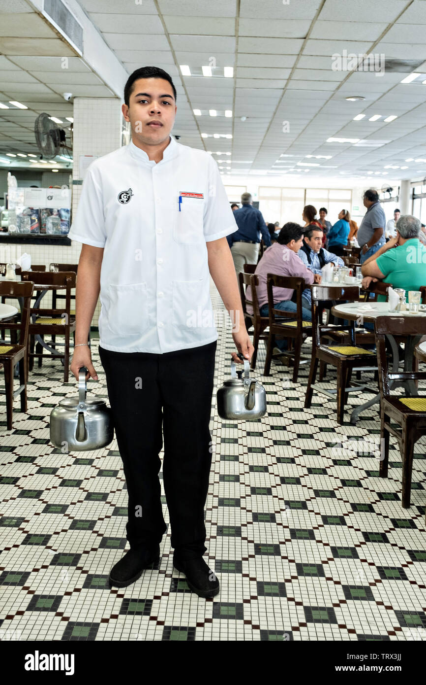 Une offre est titulaire d'un pot de café chaud et un de lait chaud qu'il attend un client d'appuyer sur leur glace à l'emblématique Gran Café de la Parroquia le long du Malecon à Veracruz, Mexique. Le café est connu pour leur verse du café chaud voie lactée appelée lechero qu'ils ont servis depuis 1808 et dans leur forme actuelle a fonctionné sans interruption depuis 1926. Banque D'Images