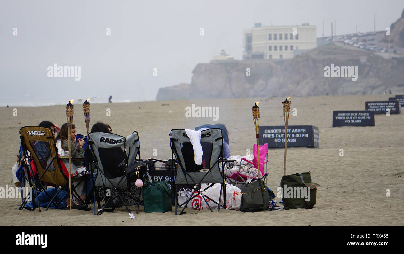 Les amis se sont rassemblés sur la plage de l'océan avec des chaises et des torches tiki en un jour brumeux. Cliff House dans l'arrière-plan. San Francisco, California, USA Banque D'Images