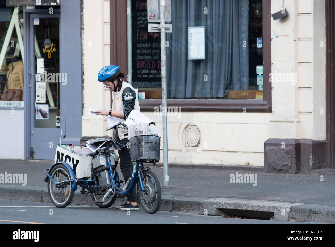 Tôt le matin dans la région de Fitzroy, à Melbourne, en Australie, une femme se tient près de la batterie d'powered tricycle et vérifie la paperasse pendant un run de livraison de journaux Banque D'Images