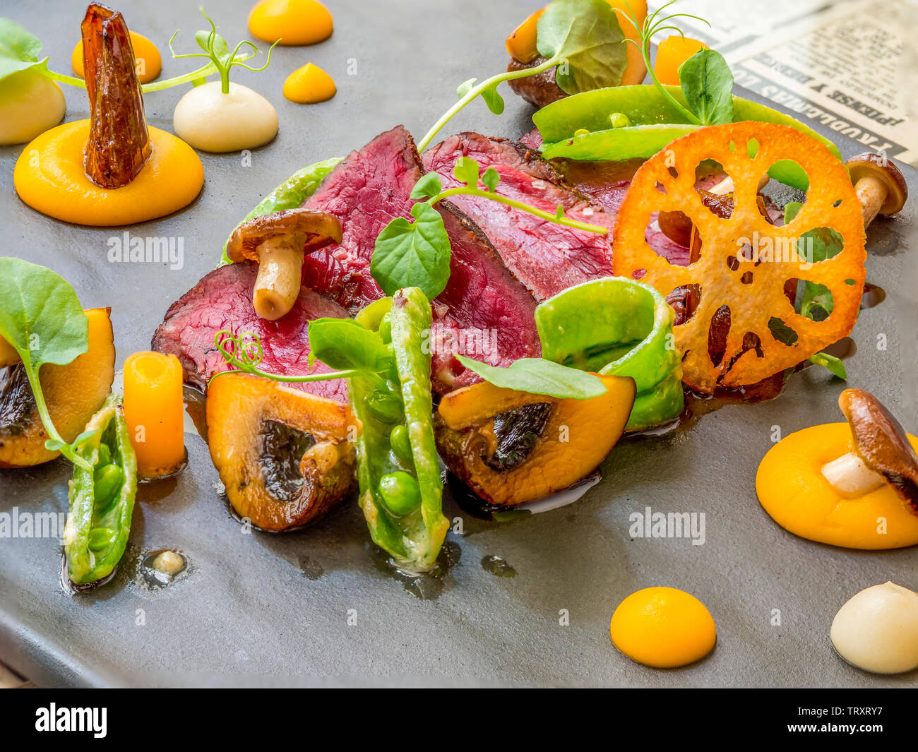 Steak de bœuf de taille moyenne à rare en tranches gastronomiques avec champignons sauvages, croustilles de racine de Lotus et purée de carottes sur une assiette d'ardoise Banque D'Images
