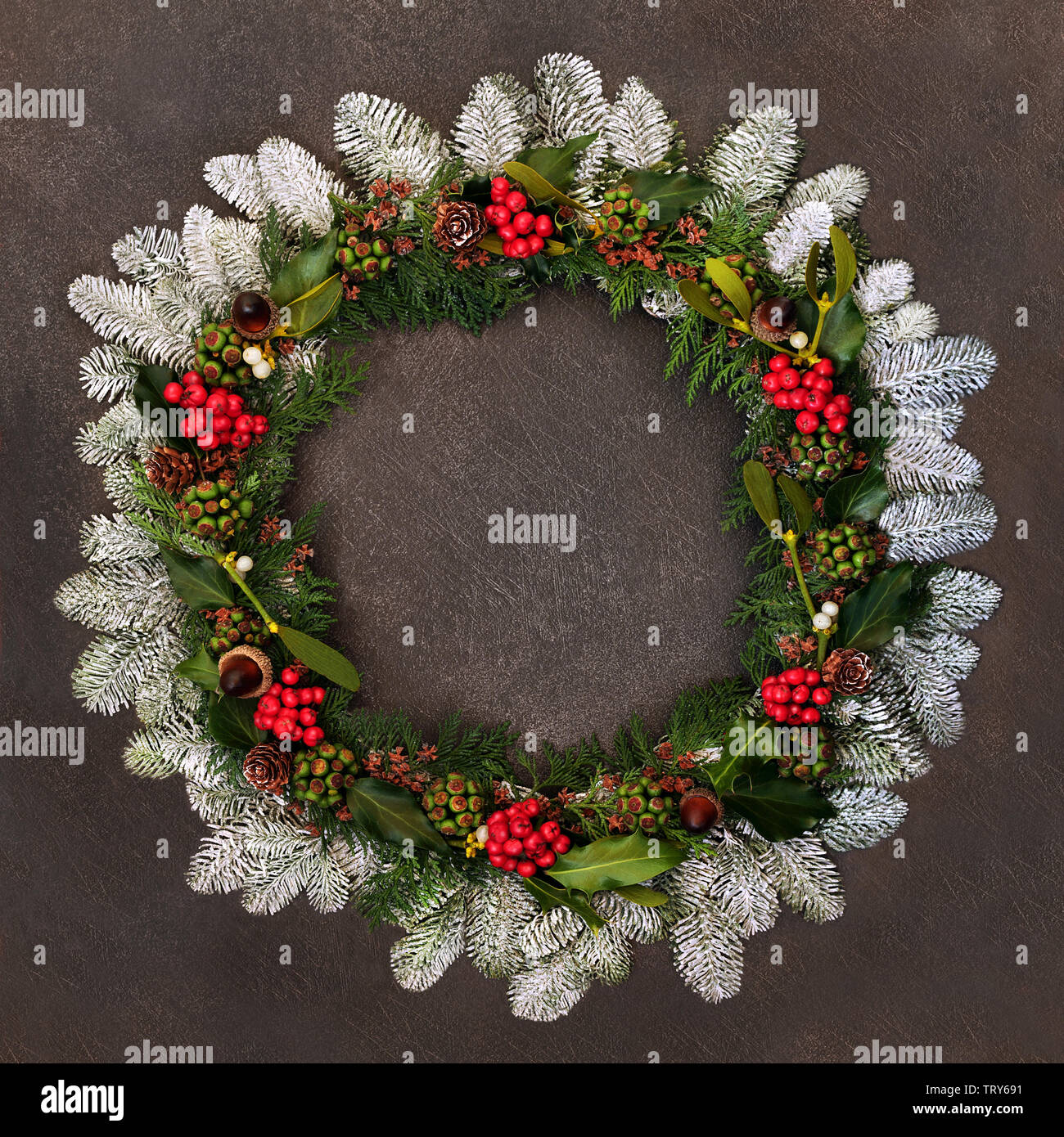Hiver naturel et couronne de Noël avec le houx, le lierre, le gui, le sapin couvert de neige, les glands, pommes de pin et feuilles de cèdre sur grunge background. Banque D'Images Hiver naturel et couronne de Noël avec le houx, le lierre, le gui, le sapin couvert de neige, les glands, pommes de pin et feuilles de cèdre sur grunge background. Banque D'Images