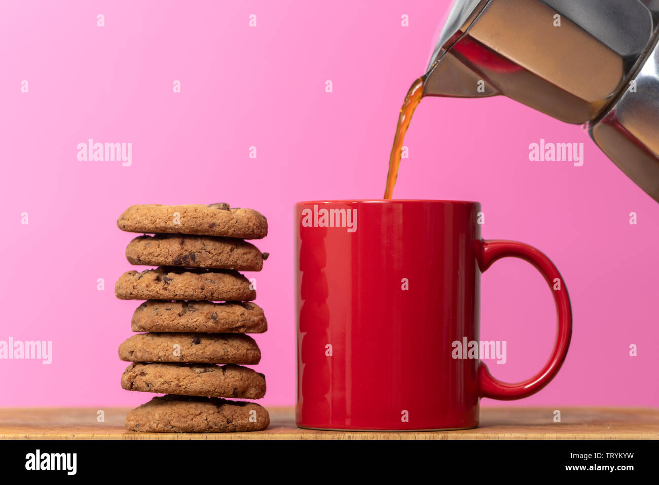 L'on verse du café une tasse rouge int avec une pile de cookies aux pépites de chocolat Banque D'Images