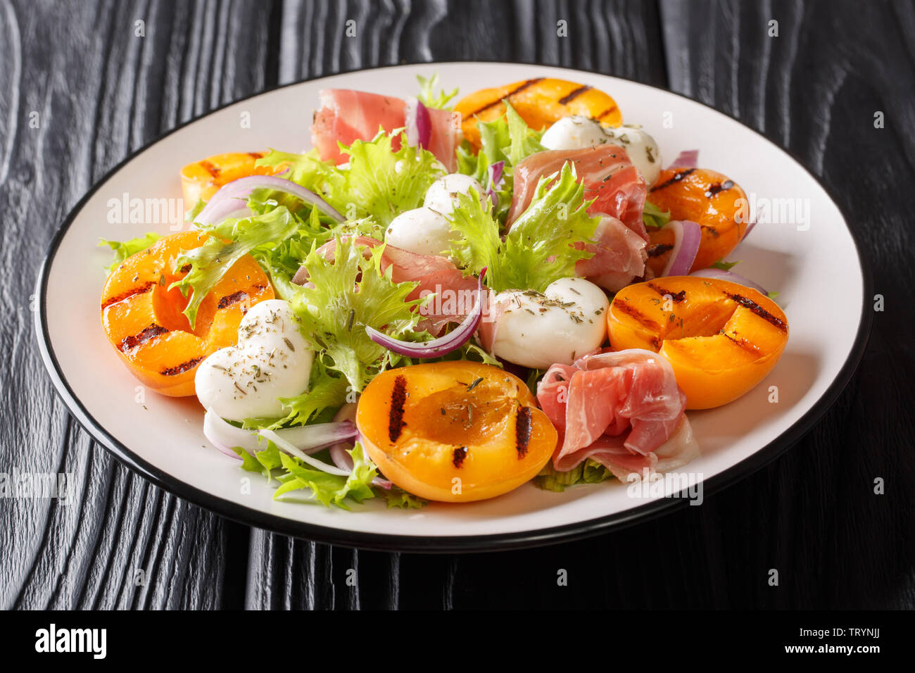 Recette facile pour l'été salade avec fromage mozzarella, prosciutto, abricots grillés, oignons rouges et la laitue sur une assiette sur la table. horiz Banque D'Images