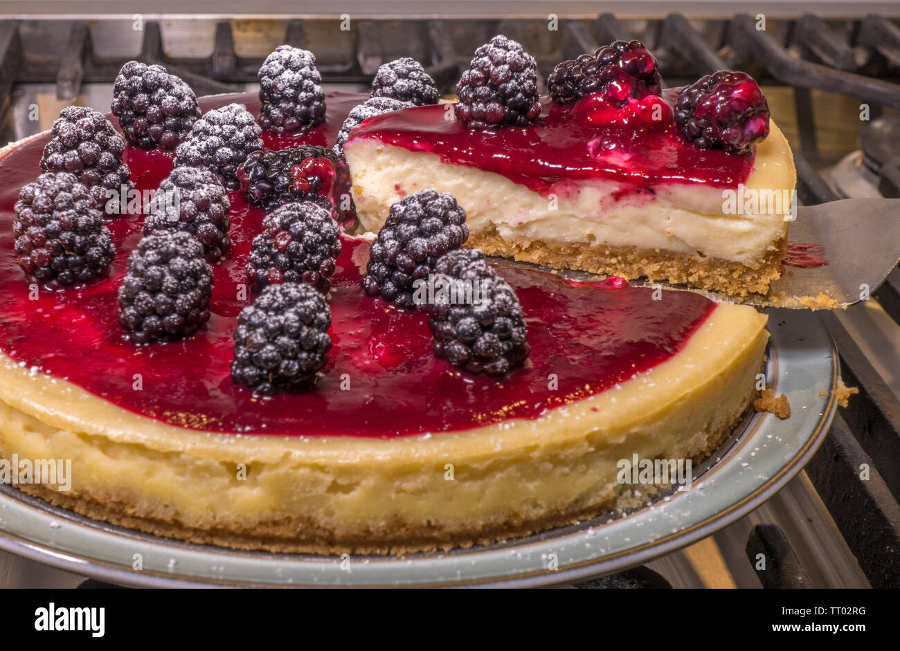 Une coupe triangulaire a été levé à partir d'un ensemble, circulaire, gâteau au fromage avec coulis de mûres sur le dessus, frais du four et reposant sur une assiette. Banque D'Images