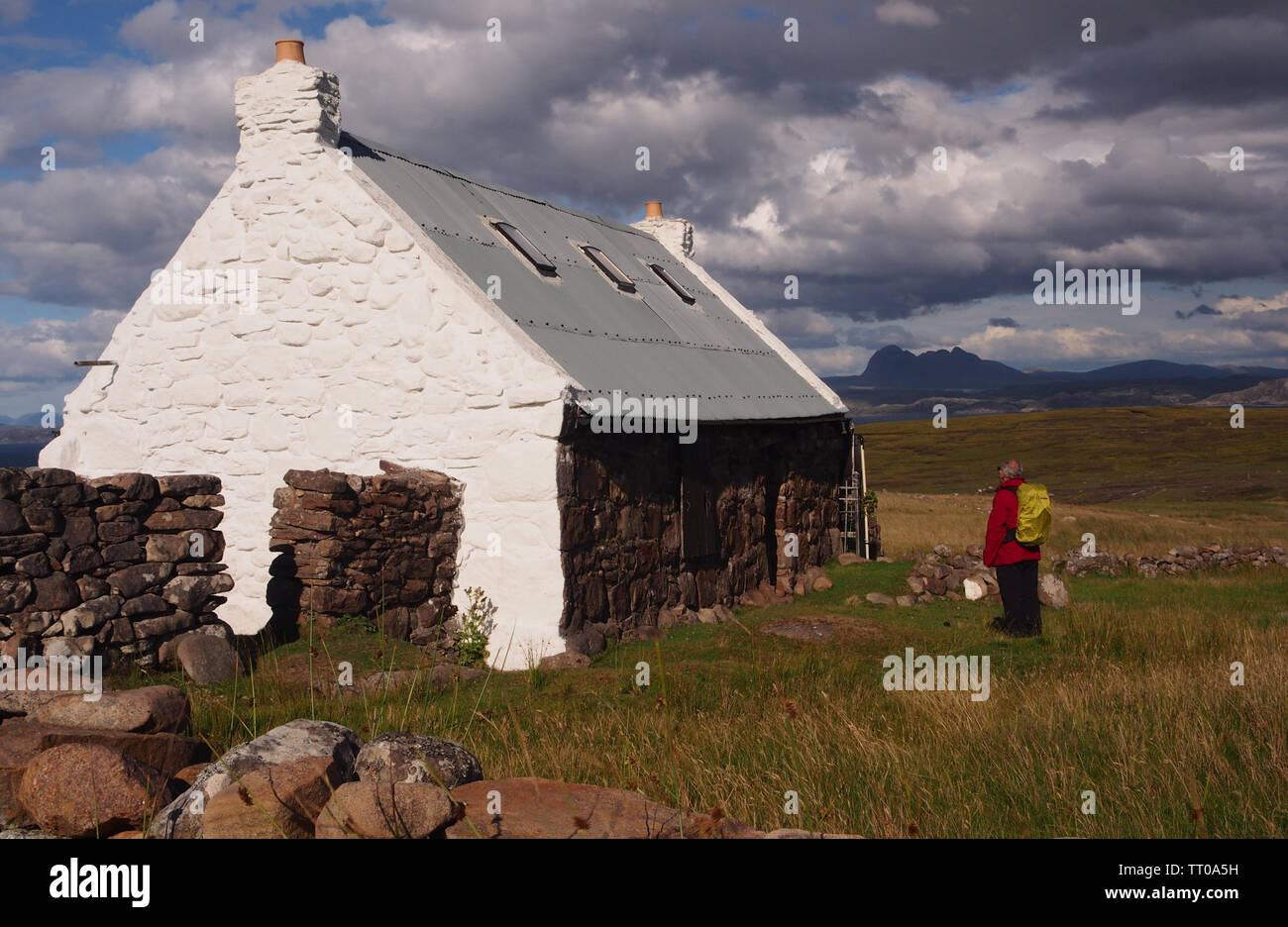 Un randonneur regardant un crofters à cottage sur la péninsule de Coigach, l'Écosse, avec les montagnes et la mer en arrière-plan et un ciel. Banque D'Images