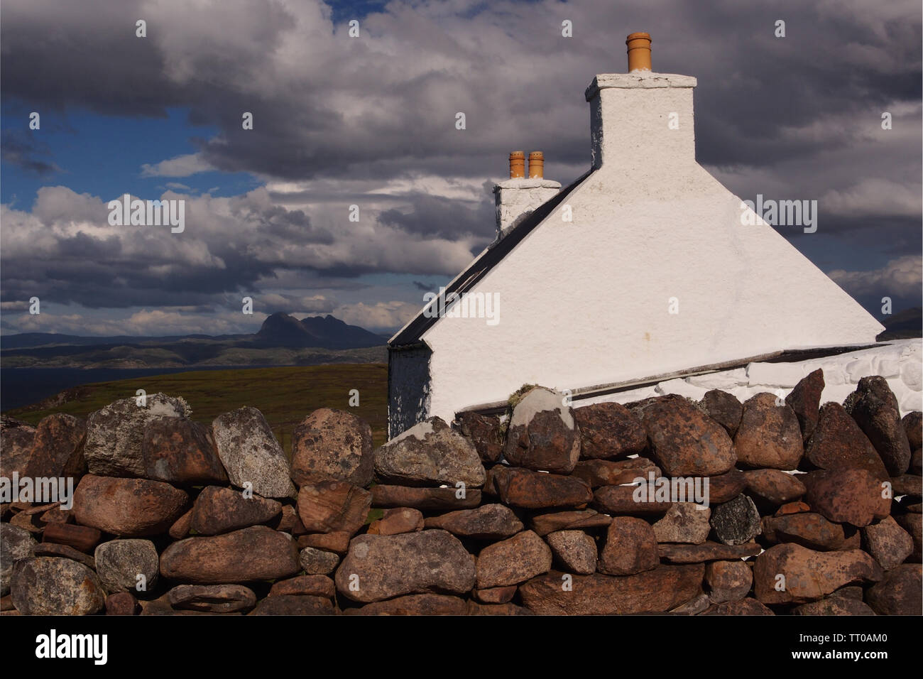Une vue sur le pignon d'une maison de vacances avec crofters à deux cheminées avec une vue sur les montagnes et la mer en arrière-plan derrière un mur en pierre sèche Banque D'Images