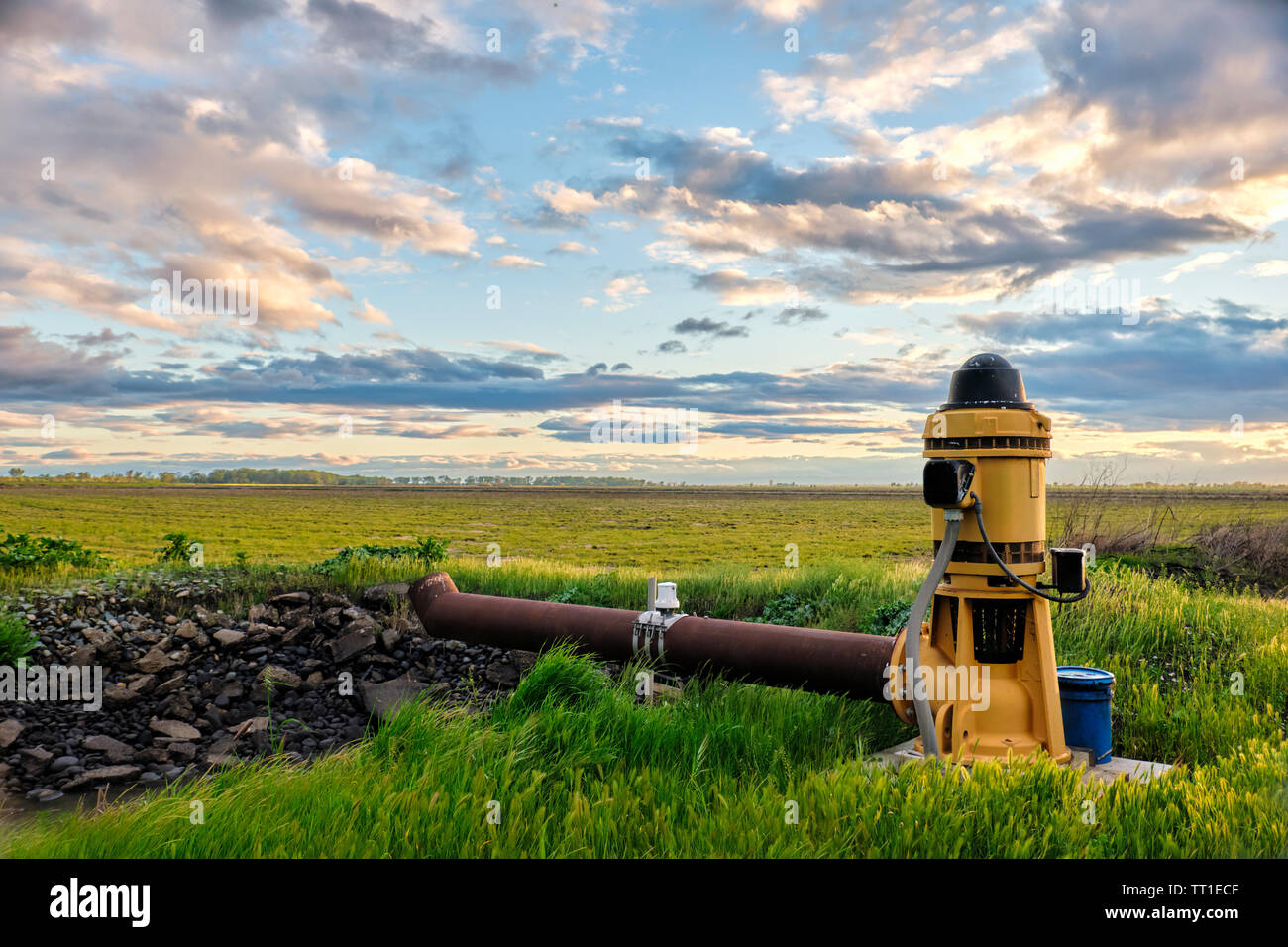 Pompe agricole sur le bord d'un champ de riz dans le cadre d'un canal beau ciel au coucher du soleil. Banque D'Images