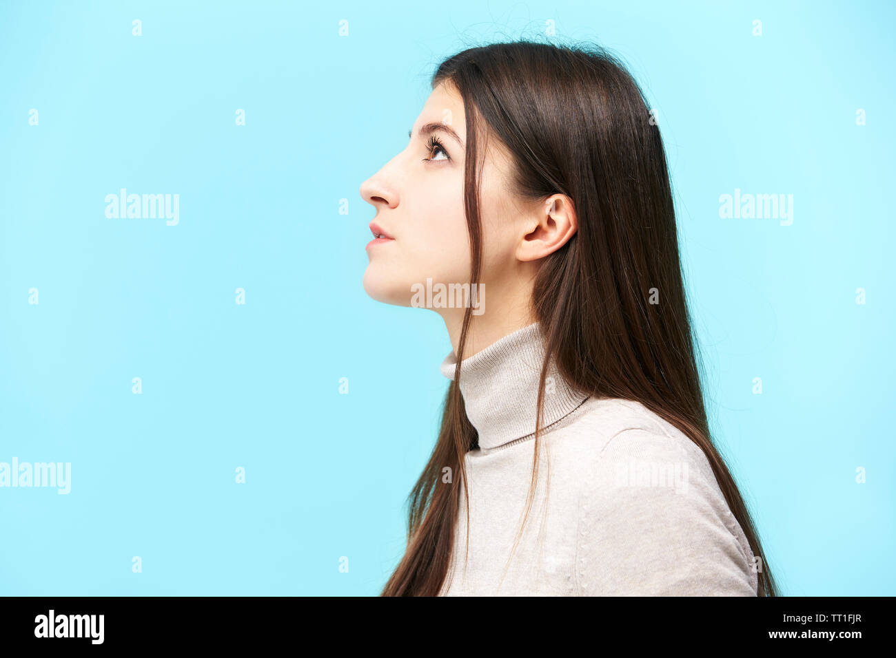 Portrait of a young woman, looking up, side view, isolé sur fond bleu Banque D'Images