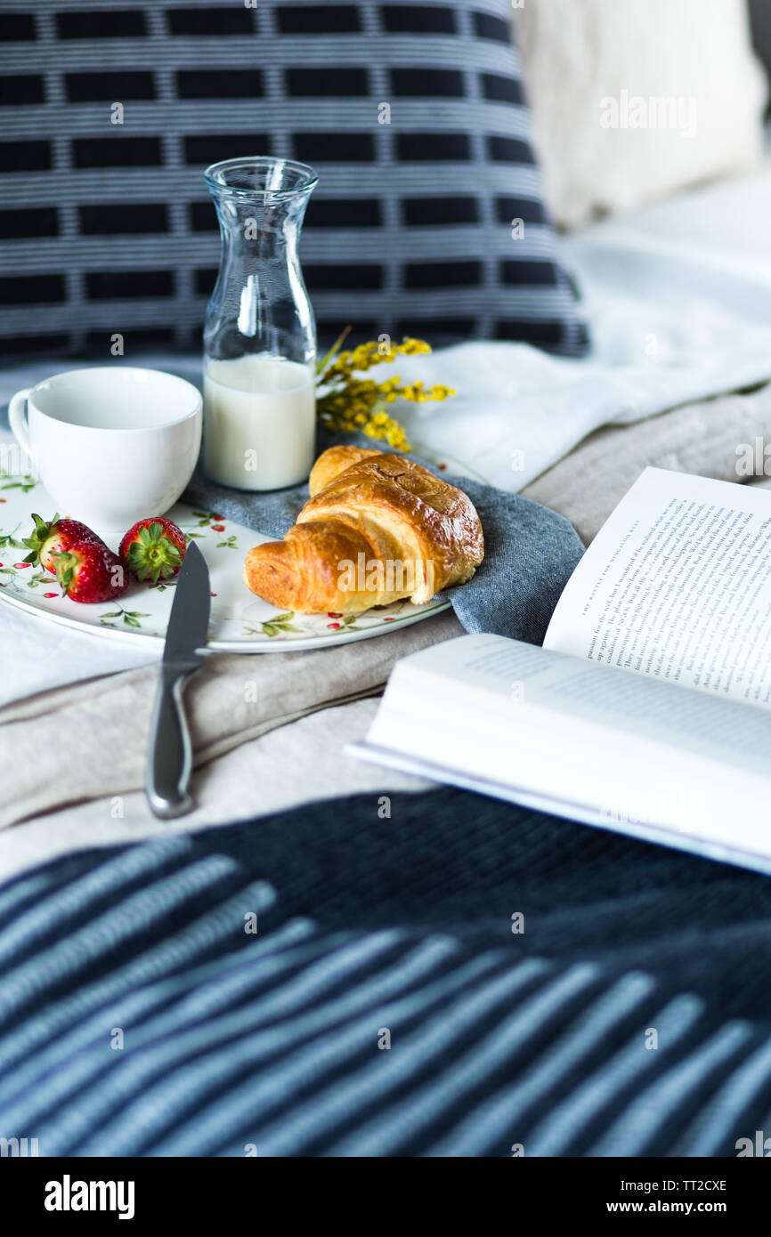 Petit-déjeuner de croissants, des fraises et du café servi au lit avec un roman ouvert Banque D'Images