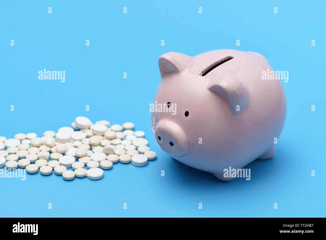 Pink Piggy Bank dans la forme d'un cochon se trouve sur la droite, sur fond bleu sur la gauche sont rondes pilules blanches. Banque D'Images
