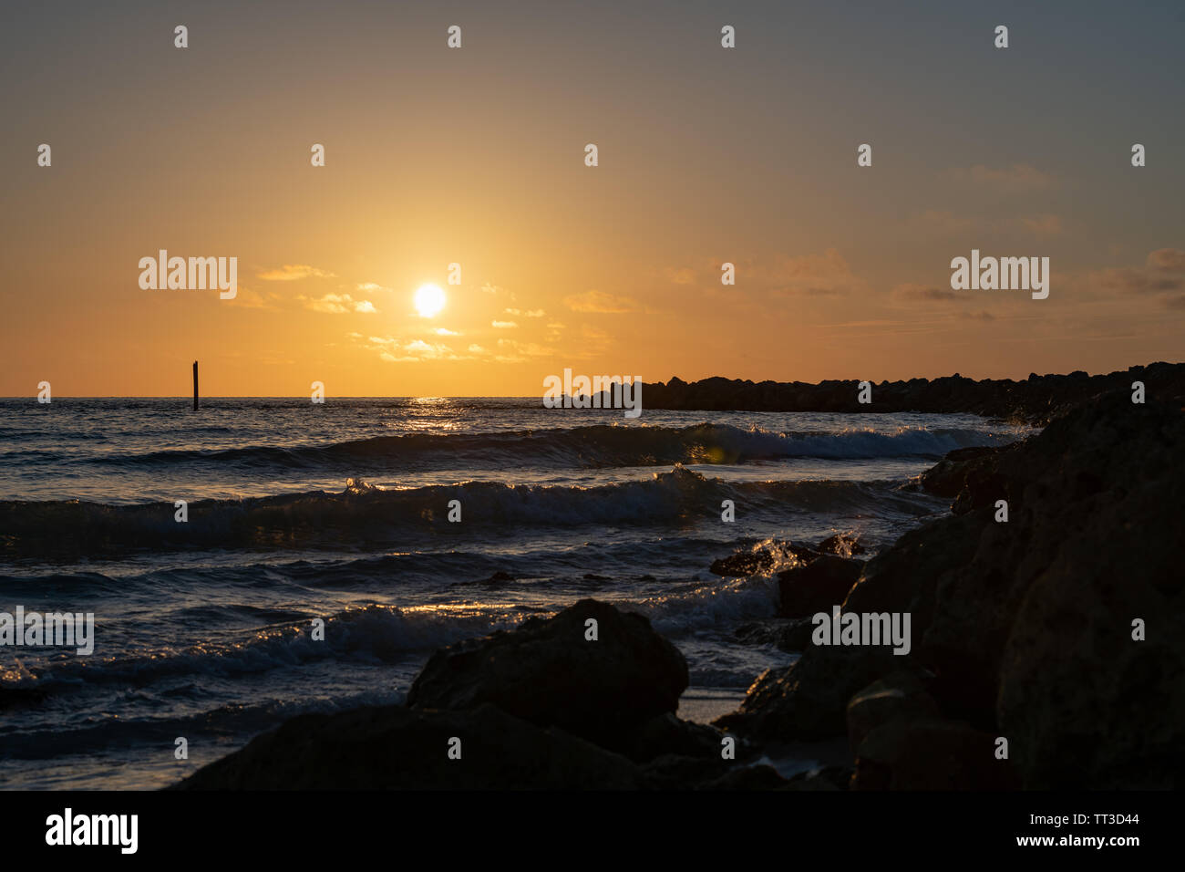 Ciel coucher de soleil à la jetée que les vagues déferlent sur les rochers Banque D'Images