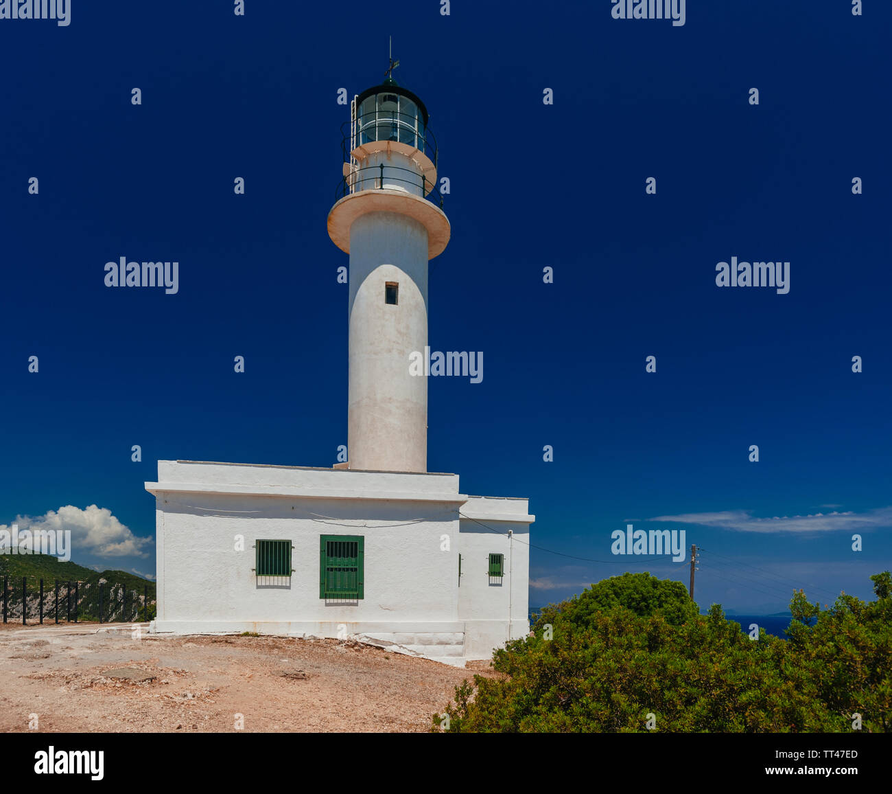 Big White lighthouse tower building debout sur terre rocheux et sablonneux avec ciel bleu profond dans l'arrière-plan Banque D'Images