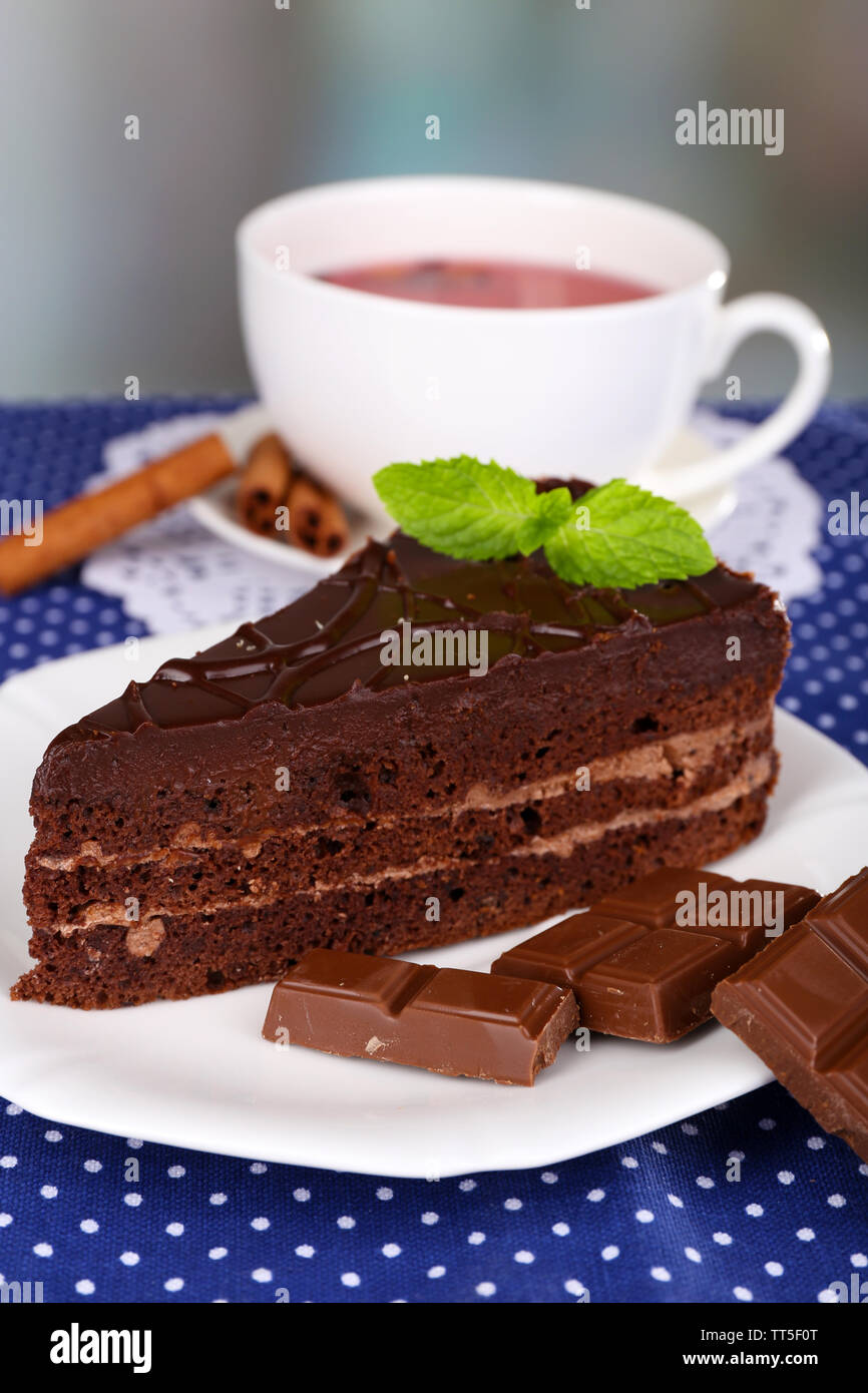 Morceau de chocolat gâteau sur une assiette et une tasse de thé sur la nappe à pois sur fond naturel Banque D'Images