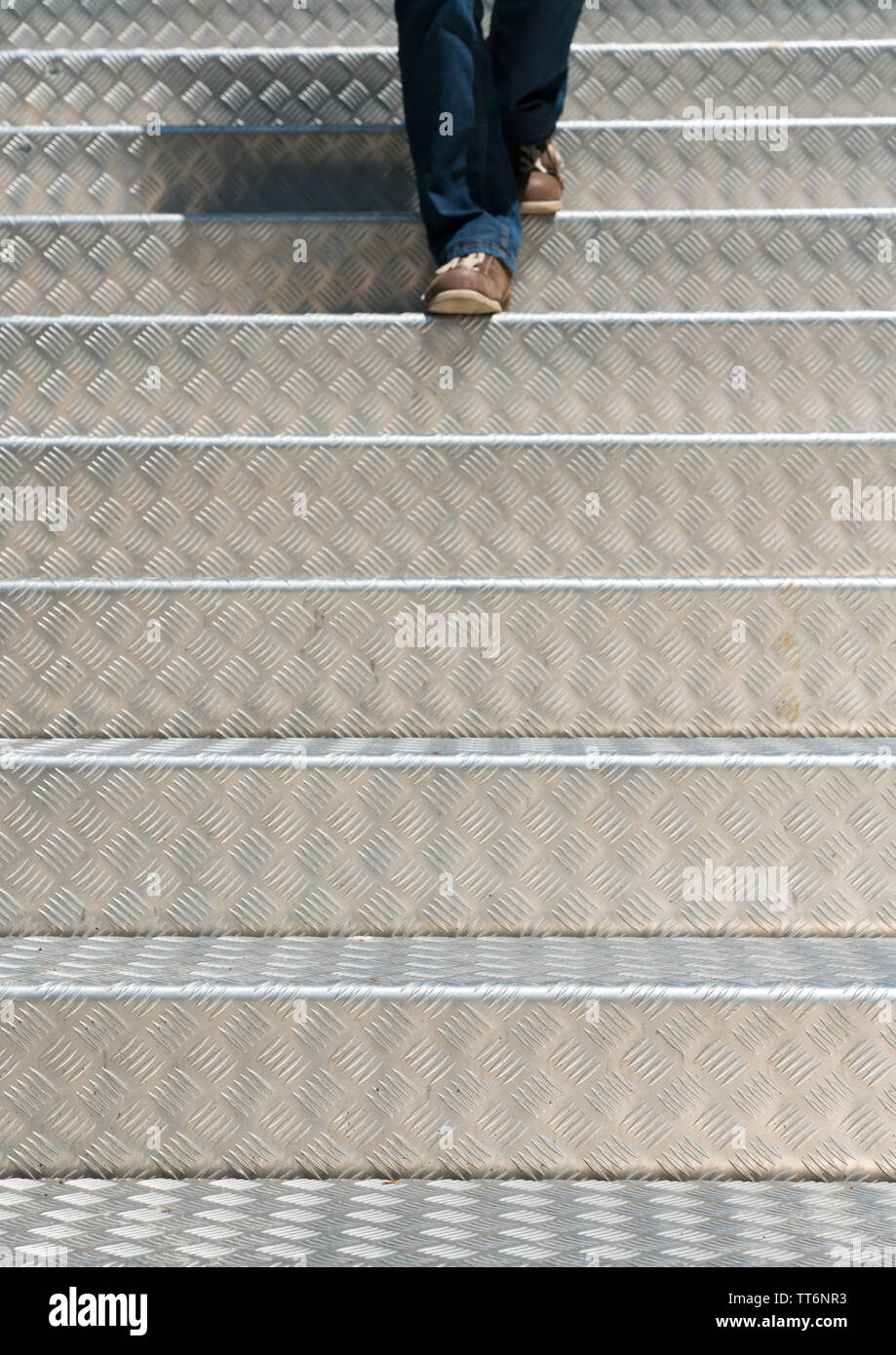 Les jambes d'une femme vêtu de jeans et portant des brown montre marchant dans la lumière vive l'aluminium d'escalier Banque D'Images