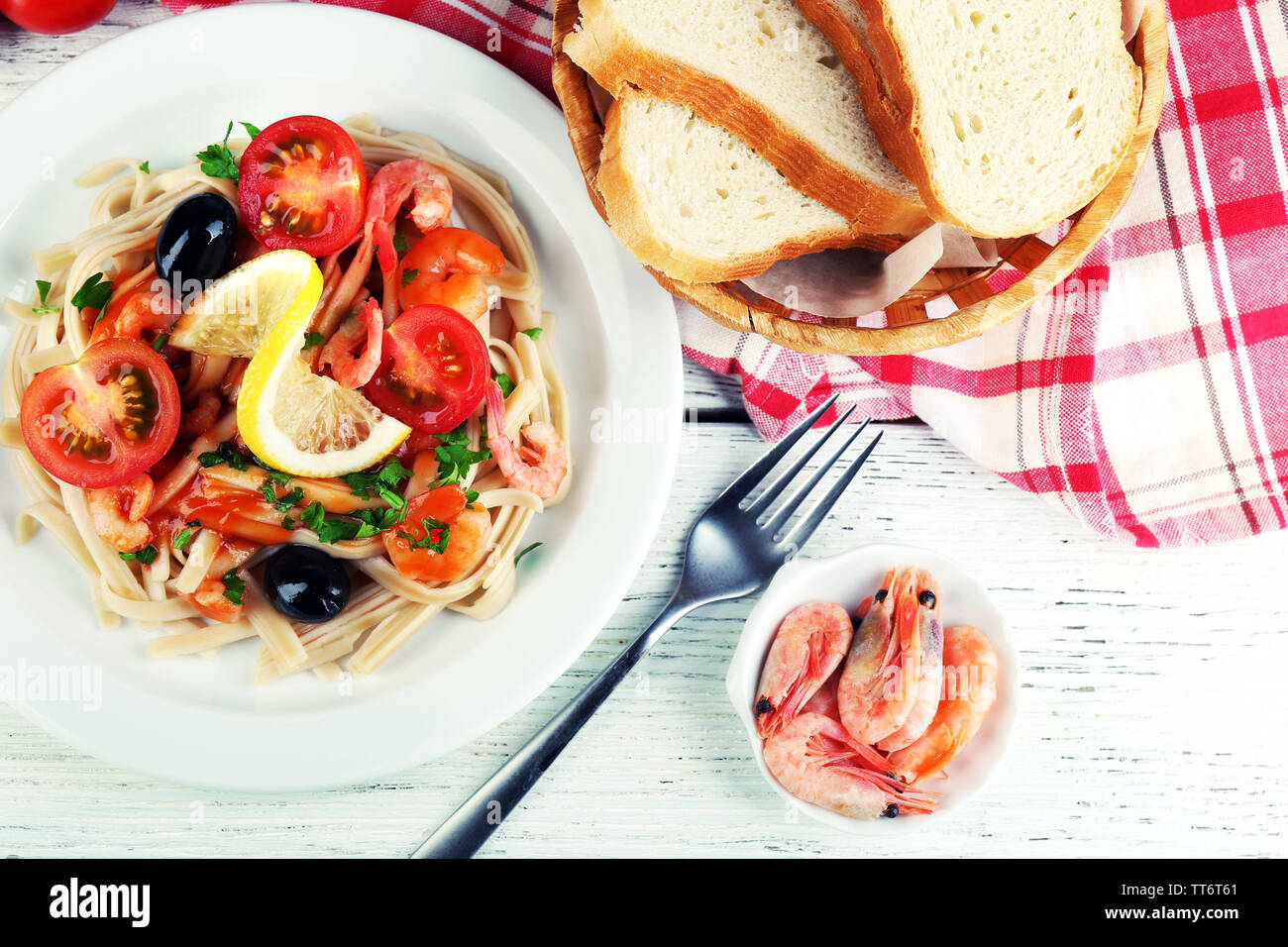 Pâtes aux crevettes, olives noires et de la sauce tomate sur la plaque sur fond de bois Banque D'Images