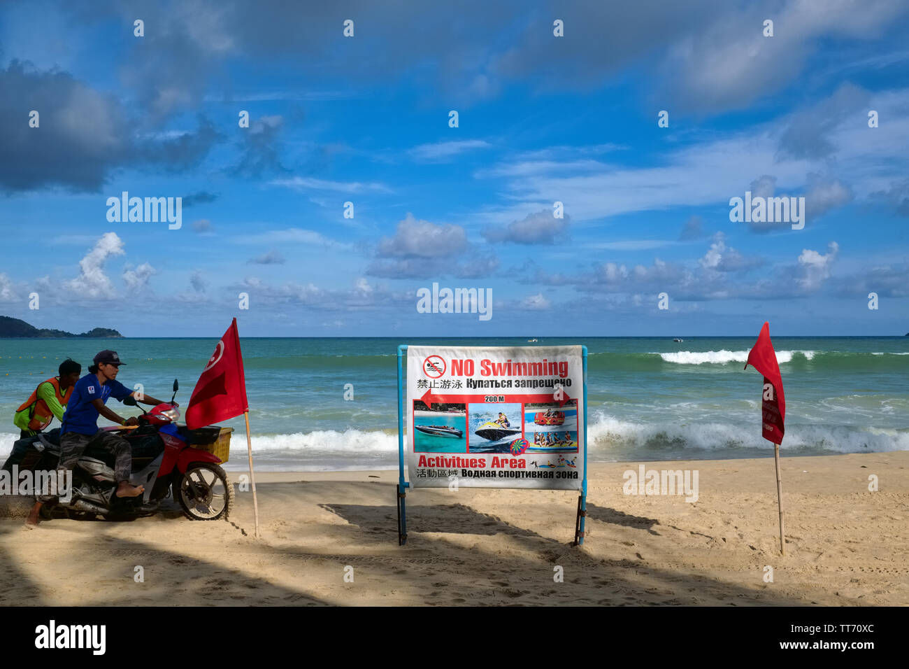 Pendant la mousson, un panneau d'avertissement à Karon Beach, Phuket, Thaïlande, interdit la baignade, tandis qu'un motocycliste tente de rouler sur le sable Banque D'Images