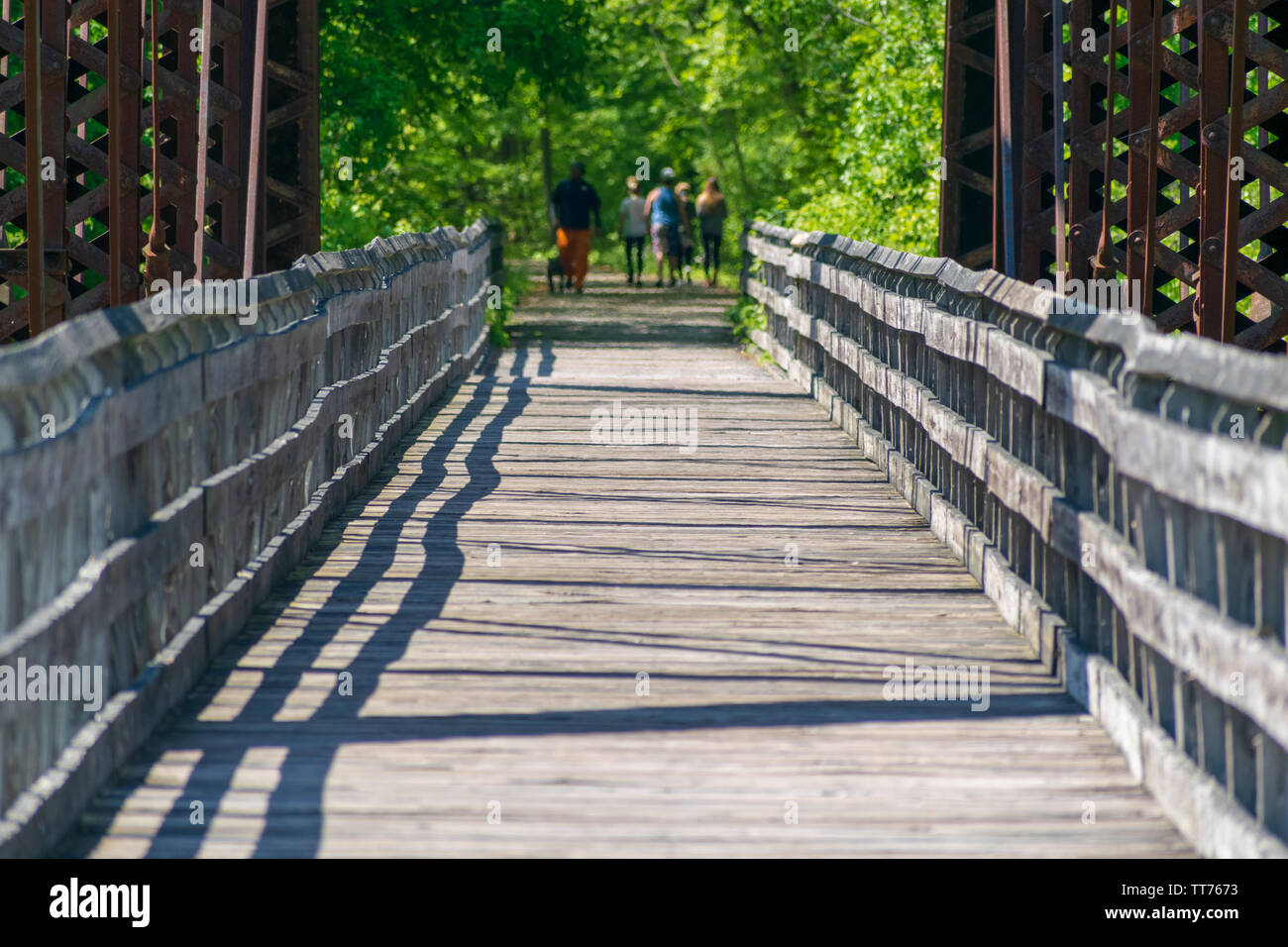Un pont piétonnier en bois menant à un sentier de randonnée à laquelle cinq adultes sont méconnaissables marche loin de la caméra. Banque D'Images