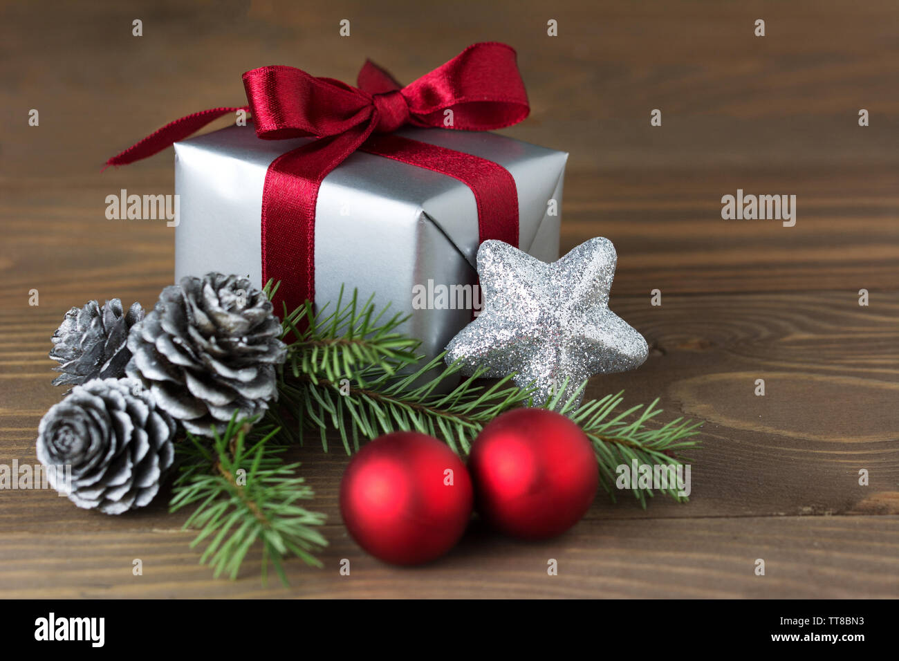 Composition de Noël : un cadeau enveloppé de ruban rouge, les cônes d'argent, boules rouges et un sapin branch - isolé sur fond de bois Banque D'Images