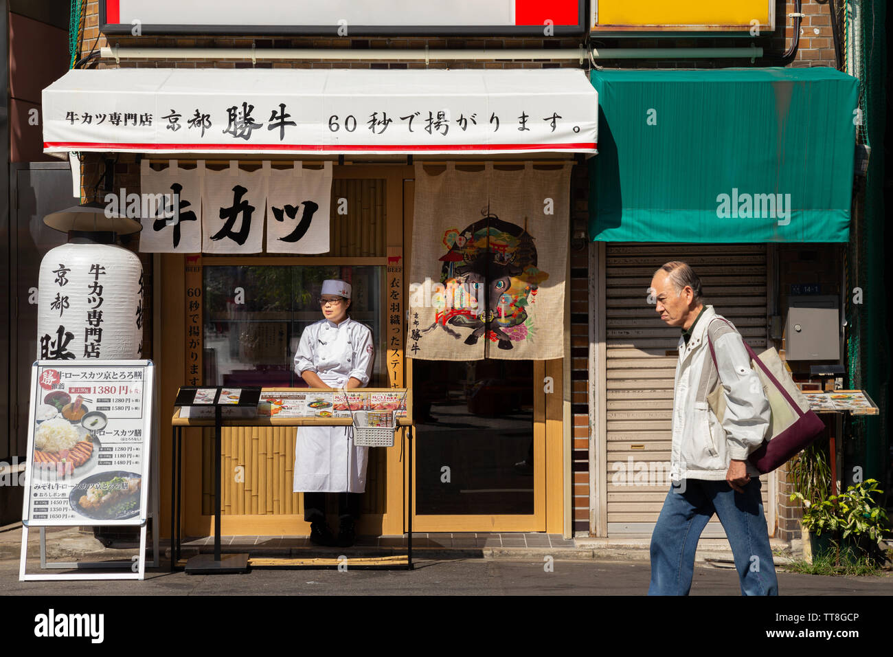 Tokyo, Japon - 18 août 2019 : old asian man marche dans la rue alors que la femme japonaise manager tente d'inviter le client à prendre le petit déjeuner ou le déjeuner Banque D'Images