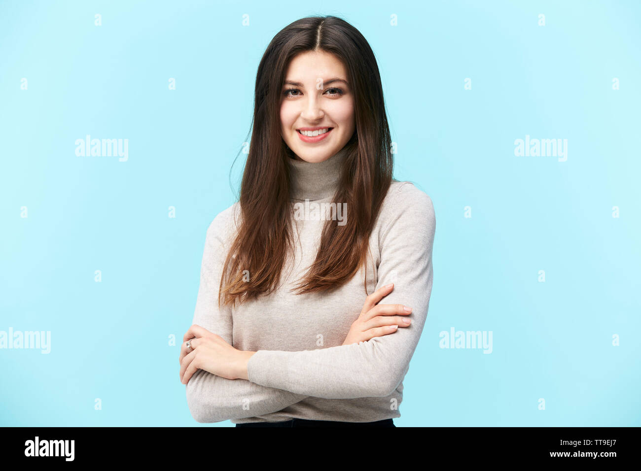 Portrait d'une belle jeune femme de race blanche, heureux et souriants, looking at camera, les bras croisés, isolé sur fond bleu Banque D'Images