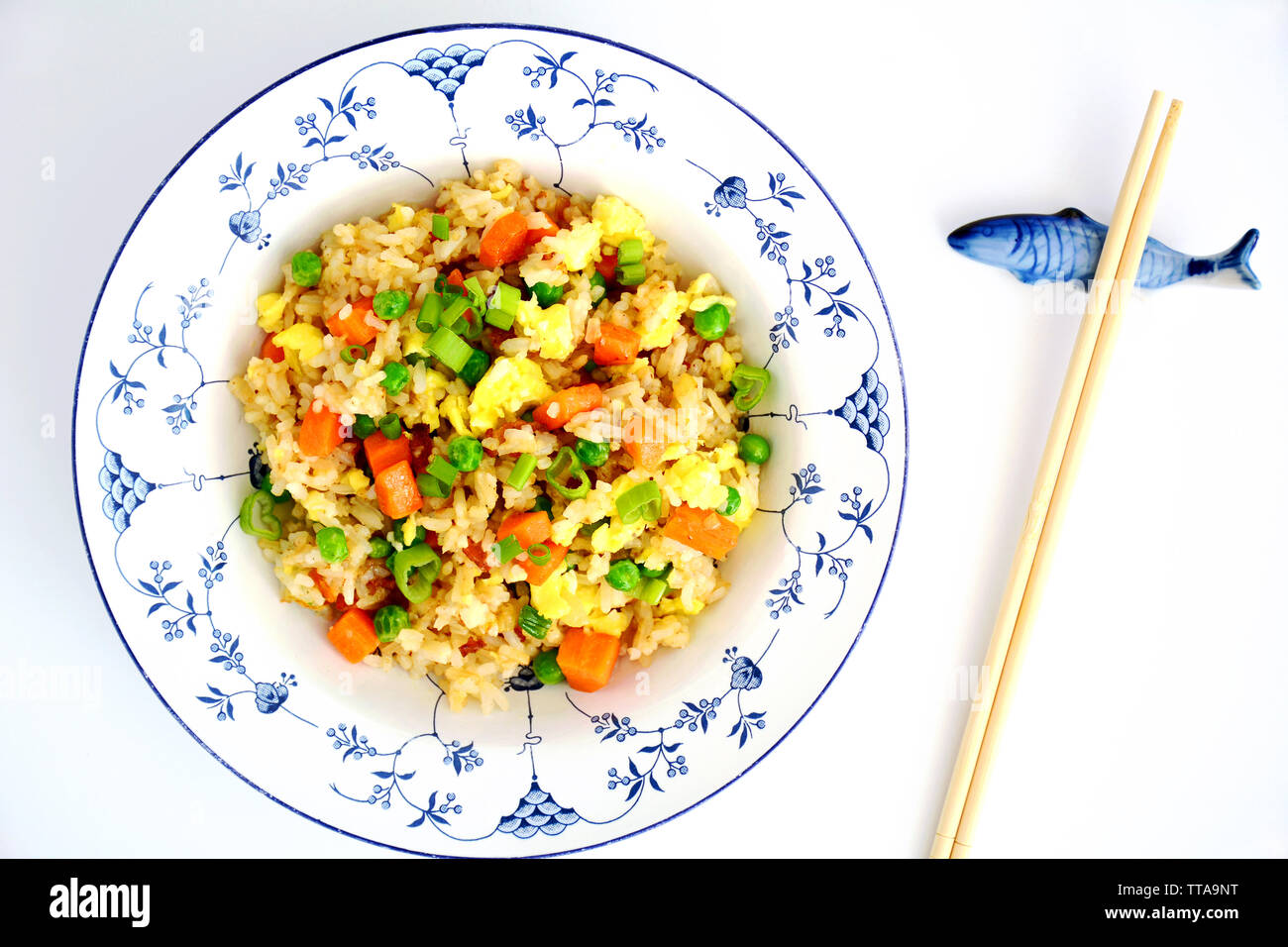 Riz frit à la maison avec bacon, oeufs, petits pois, carottes et échalottes dans joli bol bleu et blanc avec des baguettes sur les poissons en céramique reste. Banque D'Images