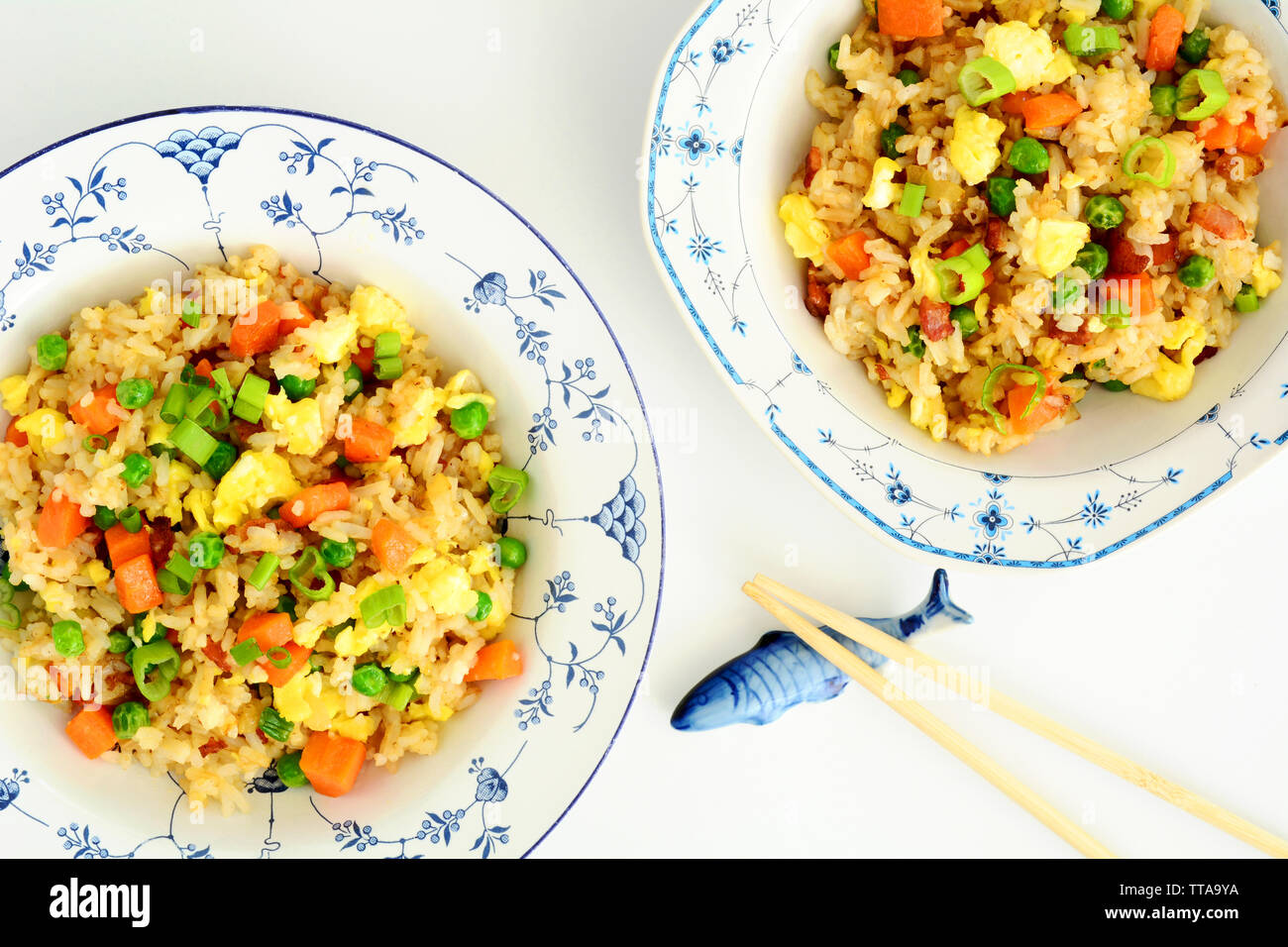 Riz frit à la maison avec bacon, oeufs, petits pois, carottes et oignons verts dans de jolis bols bleu et blanc avec chopstics sur poisson en céramique reste. Banque D'Images