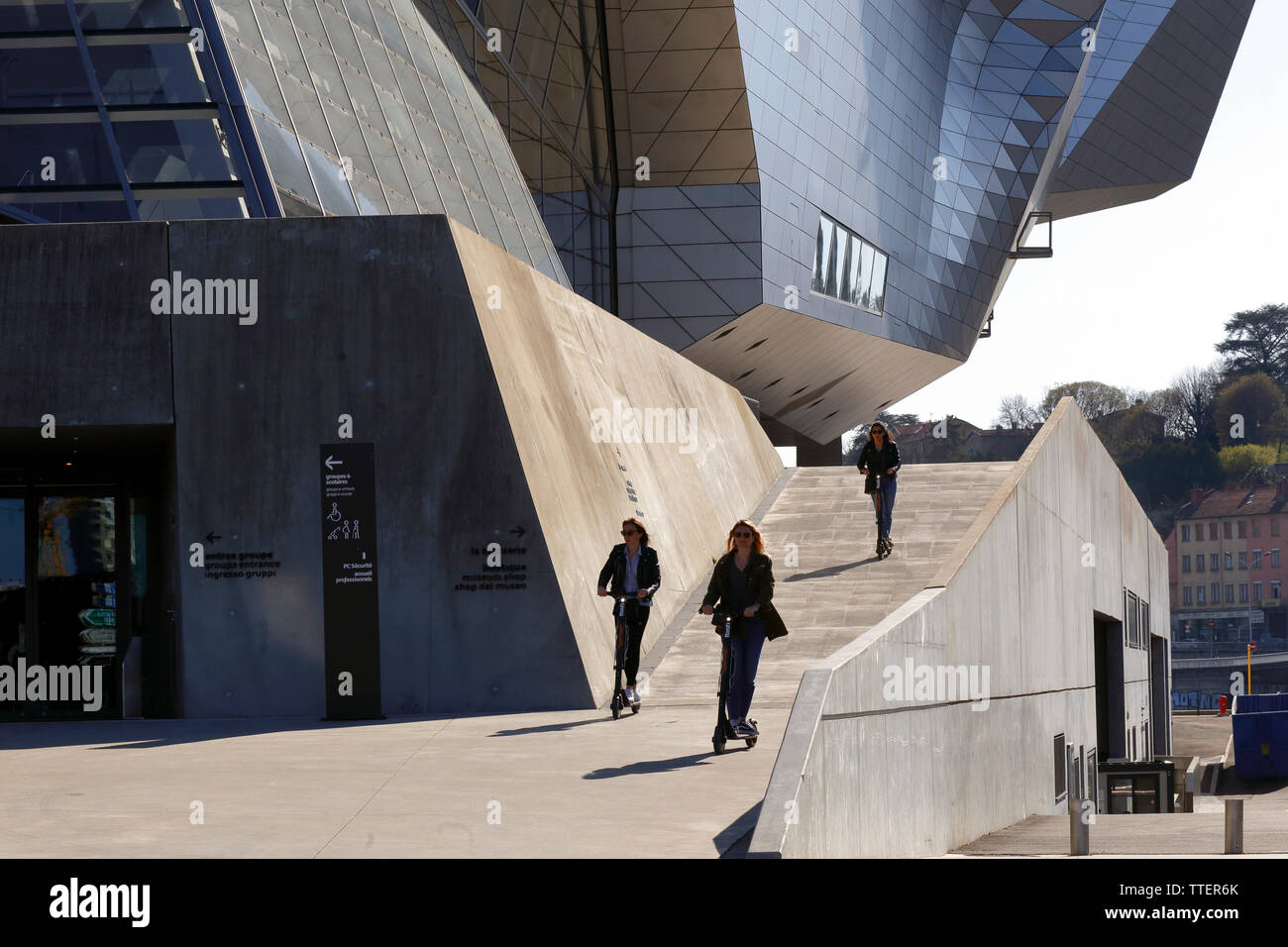 Des femmes sur des scooters électriques (trottinettes électriques) qui descendent une rampe à l'extérieur du Musée des Confluences, Lyon, France Banque D'Images