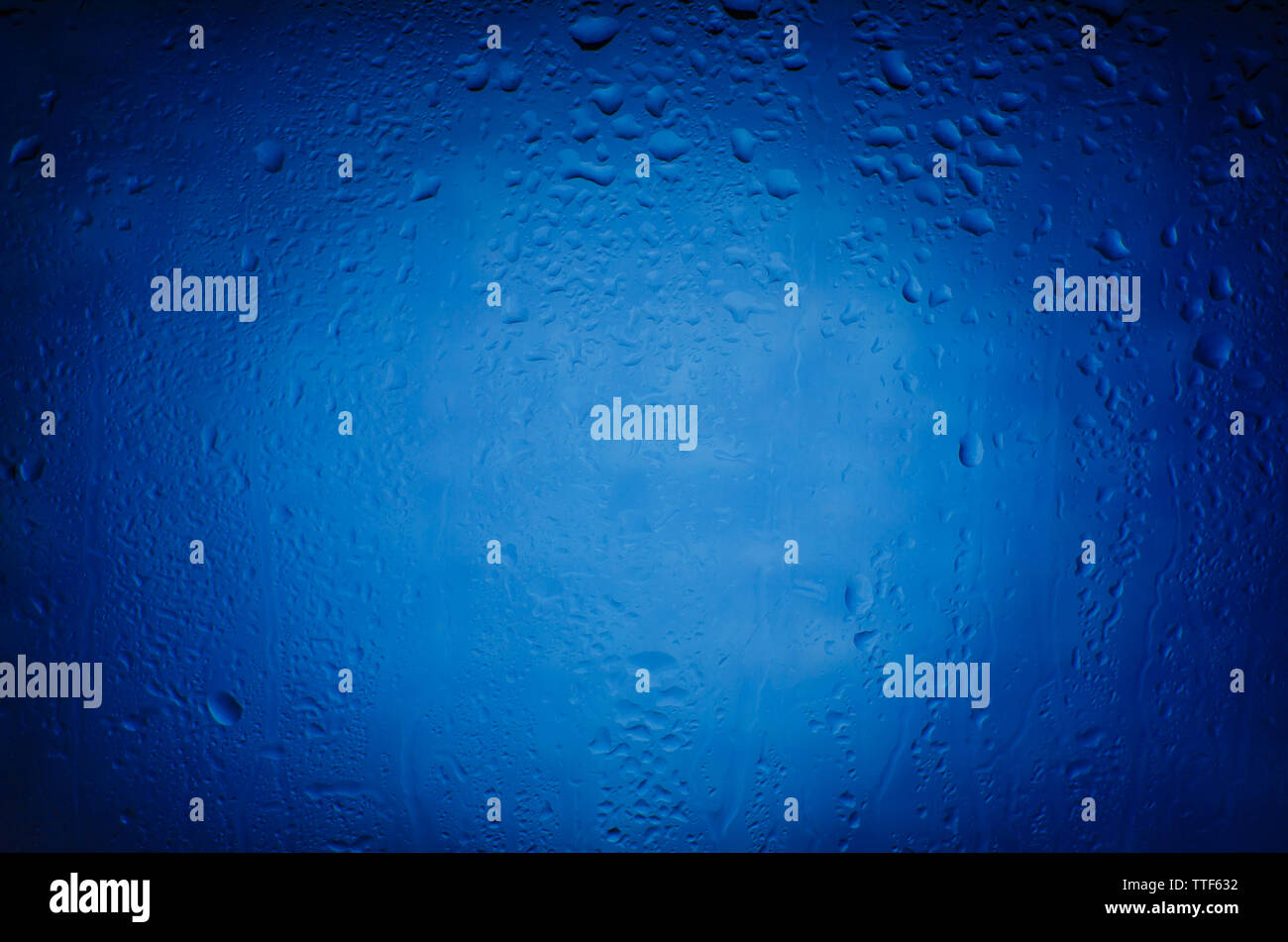 Gouttes de pluie sur le verre sur un fond bleu avec le vignettage Banque D'Images