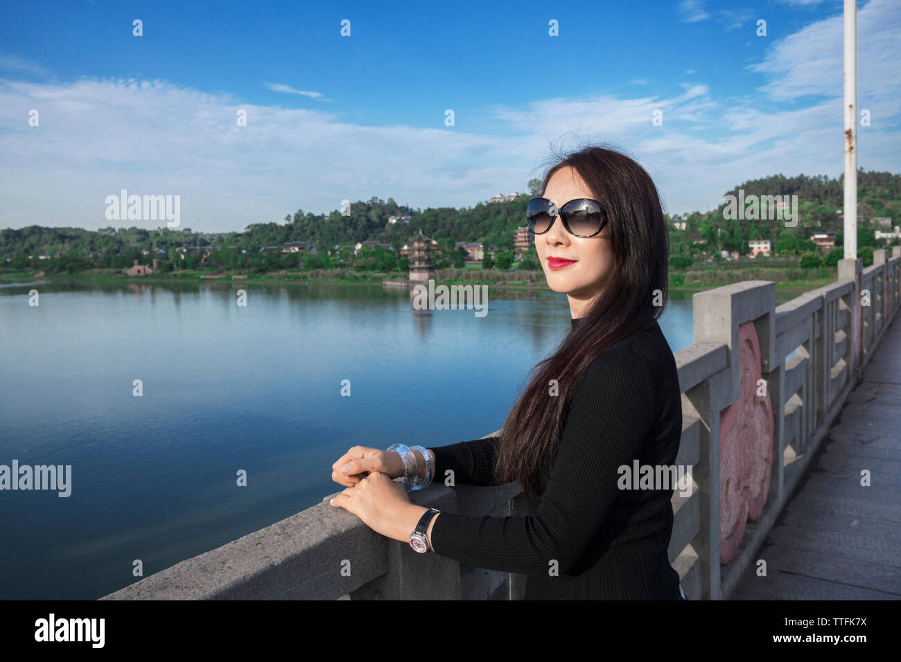 Portrait de femme portant des lunettes de soleil alors qu'il se trouvait sur la passerelle sur la rivière contre le ciel bleu Banque D'Images